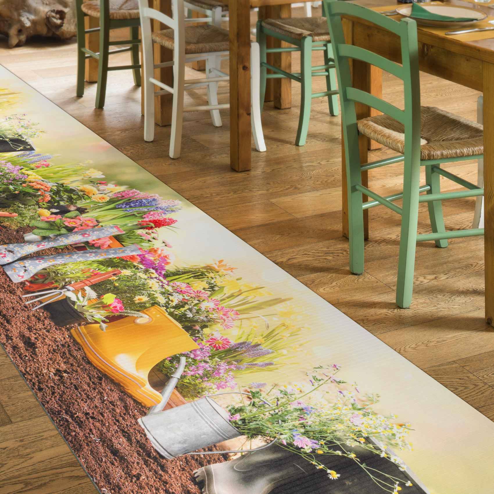 Esszimmer mit Holzstühlen um Tische herum, mit einer Boden- oder Tischgrafik mit farbenfrohen Blumen in Gießkannen und einer Gartenszene.