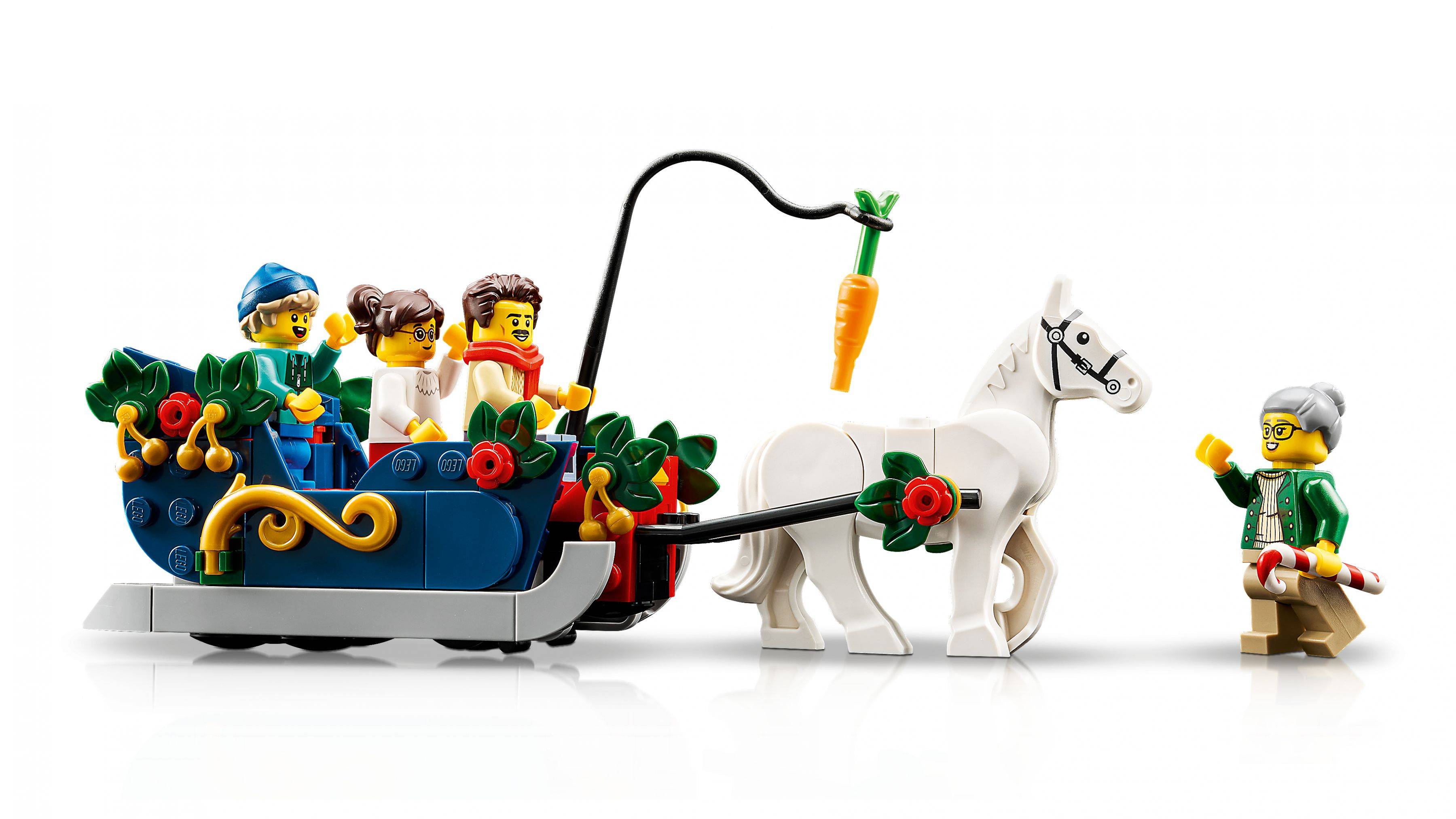 LEGO-Szenerie eines weißen Pferdes, das einen Schlitten mit mehreren Passagieren zieht, während eine Person neben ihm steht und eine Mohrrübe an einer Angelrute hält, um das Pferd zu lenken.