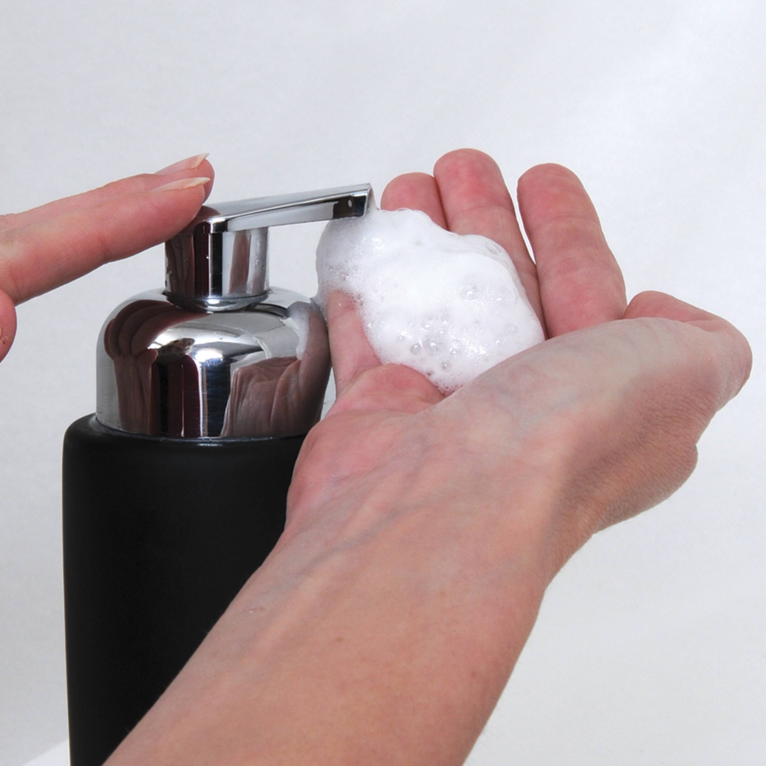 Hände, die Seifenschaum aus einer Pumpflasche in eine Handfläche verteilen.