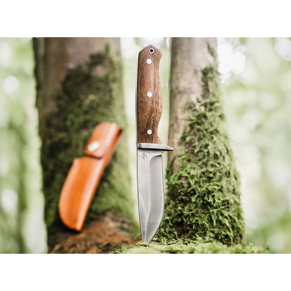 Messer mit feststehender Klinge, Holzgriff und Scheide, die an einer moosigen Baumrinde in einer Waldumgebung angelehnt ist.