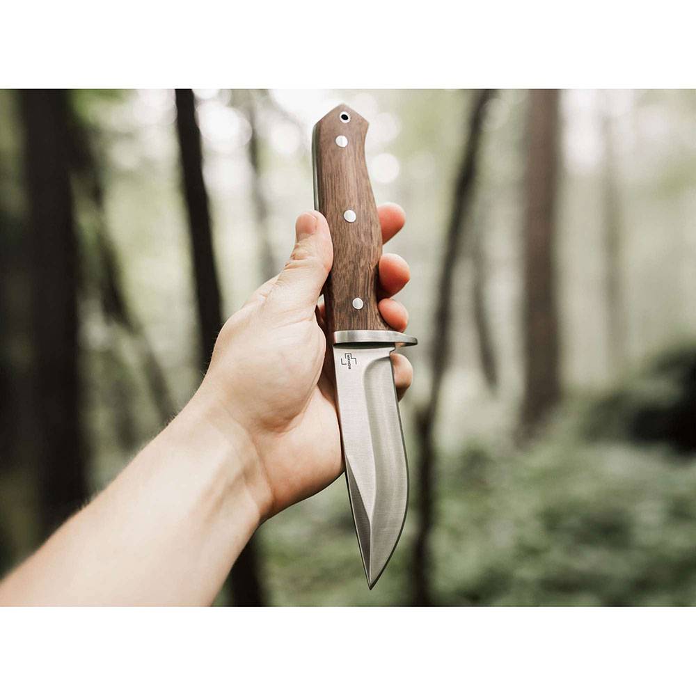 Hand hält ein feststehlendes Messer mit Holzgriff vor unscharfem Waldhintergrund.