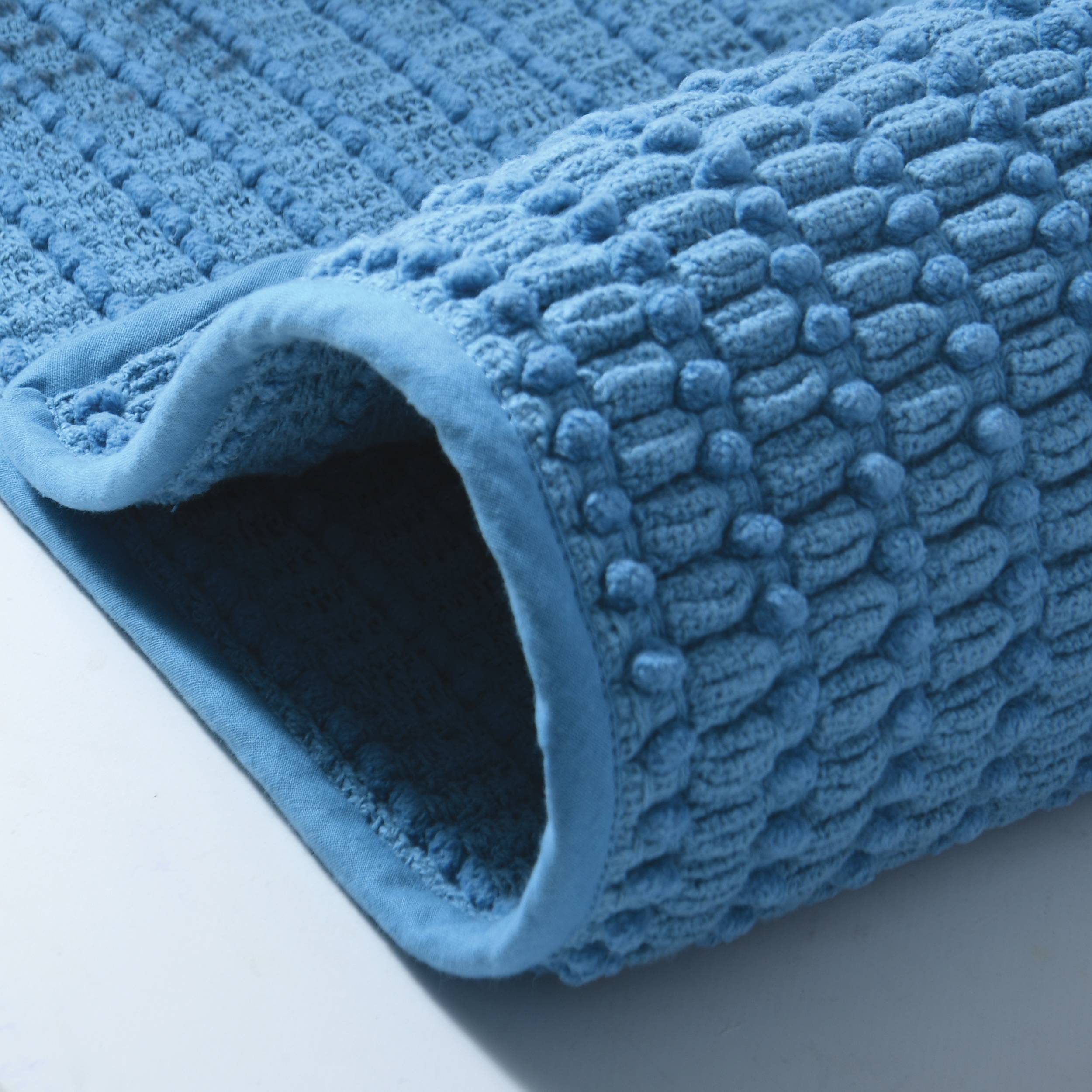 Nahaufnahme einer blauen strukturierten Badmatte oder eines Handtuchs, aufgerollt, um seine weiche Schlingenoberfläche und hohle Unterseite zu zeigen.