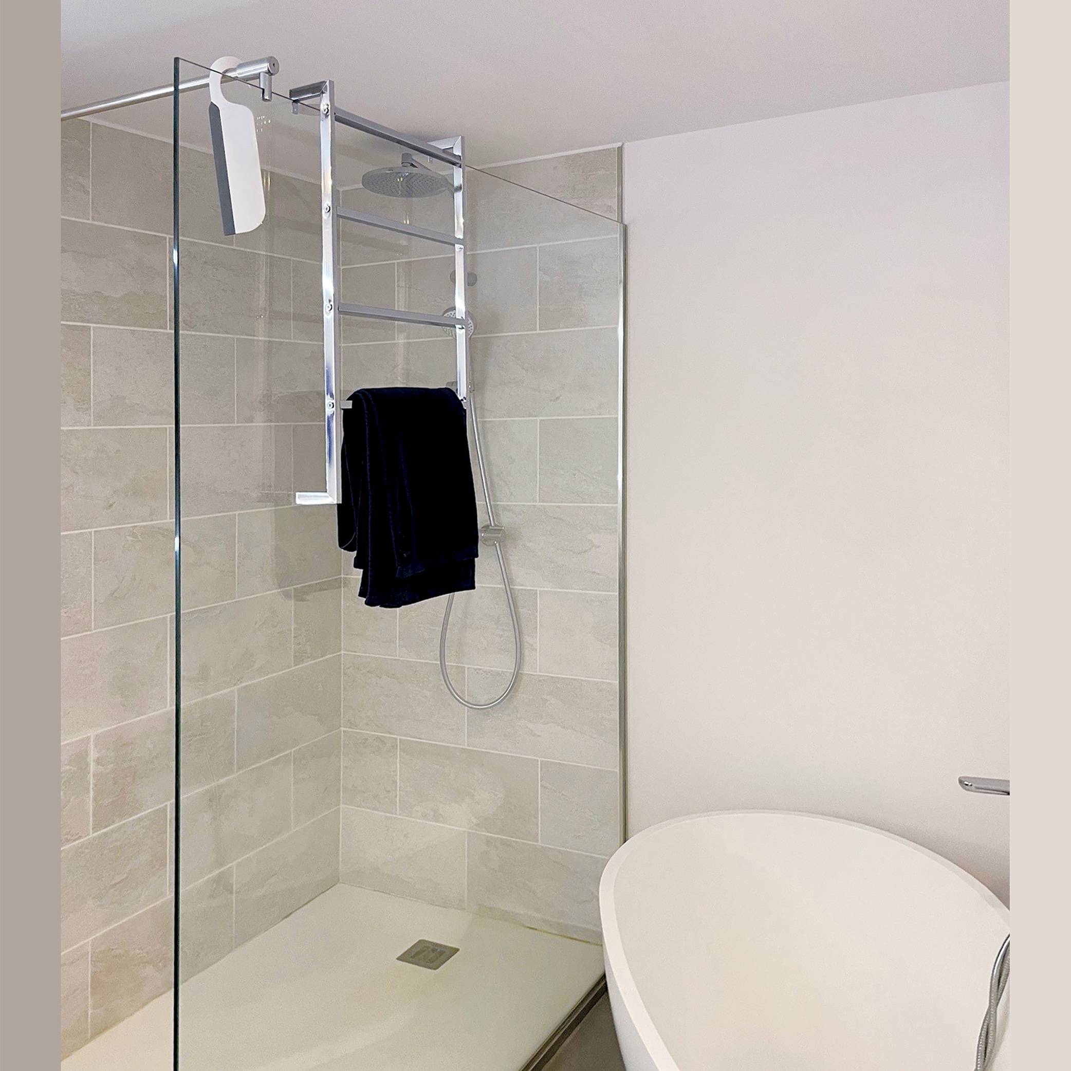 Modernes Badezimmer mit Dusche mit Glasabschluss, Chrom-Handtuchhalter mit dunklen Handtüchern und einer weißen Toilette neben der Dusche.