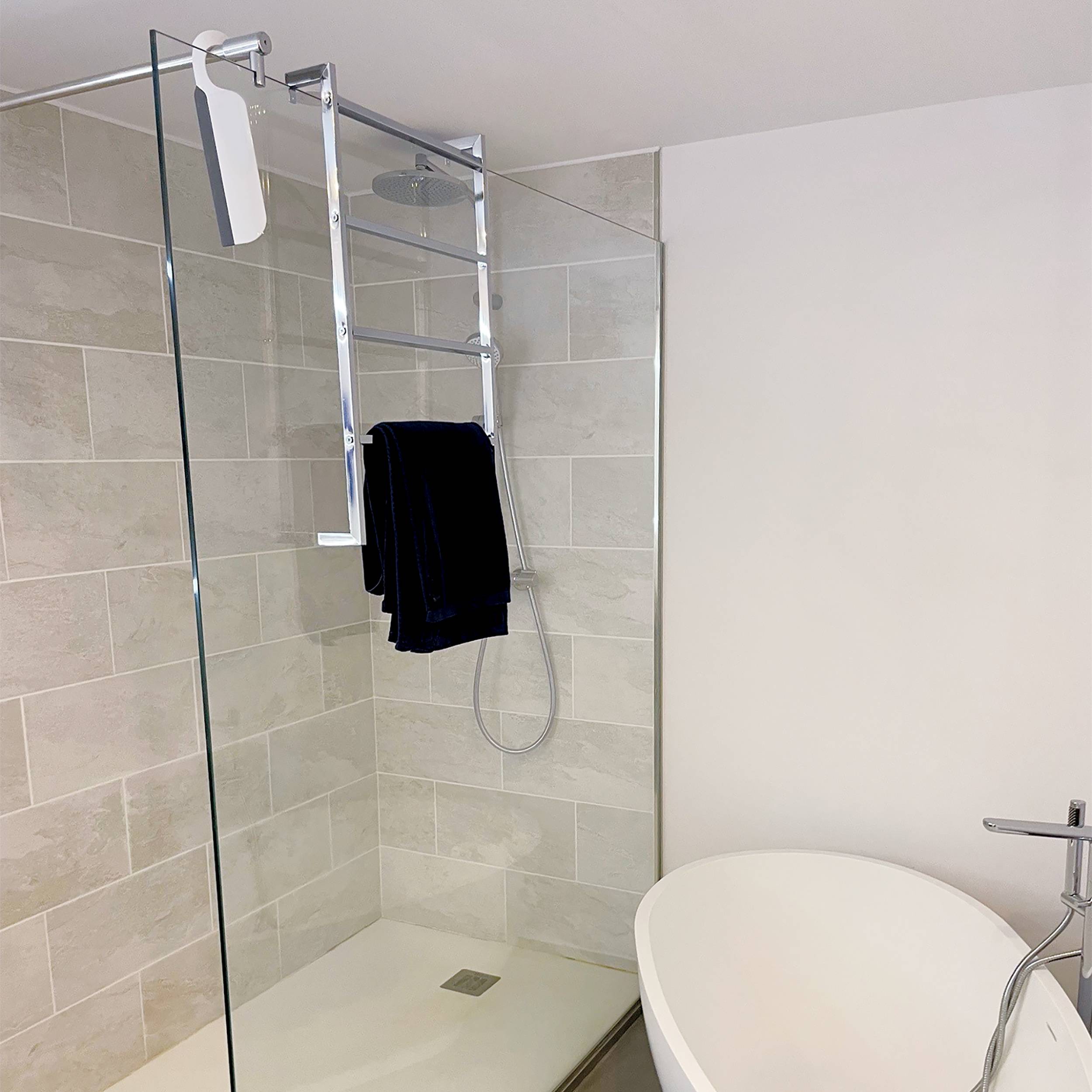 Modernes Badezimmer mit einer Dusche mit Glaseinfassung, beigen gekachelten Wänden und ein Handtuch, das auf dem Duschablage neben einer weißen Badewanne hängt.