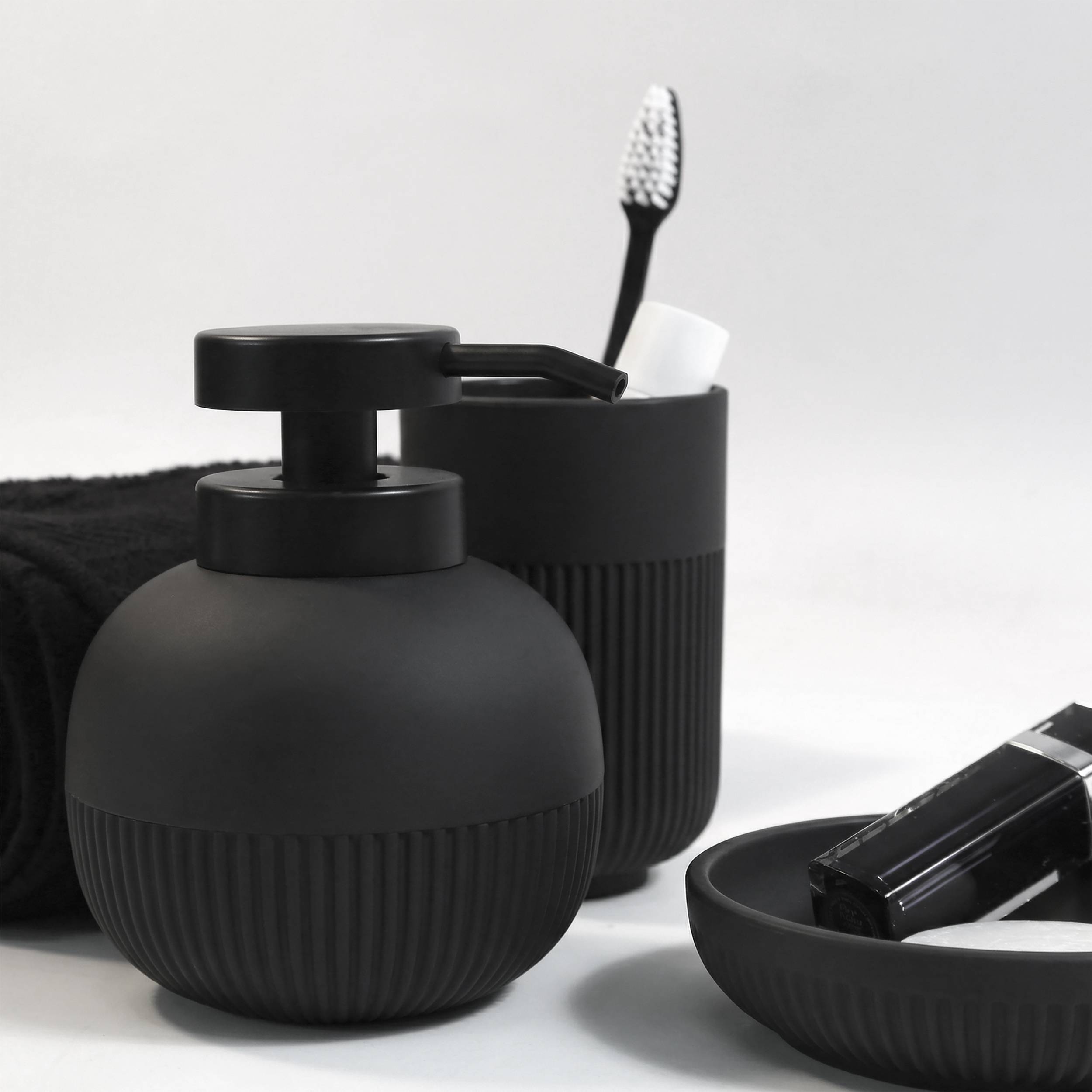 Schwarzes Badezimmerset mit Seifenspender, Zahnbürtenhalter und Schale mit einer Zahnpastatube und schwarzer Toilettenartikel-Flasche auf einer weißen Oberfläche.