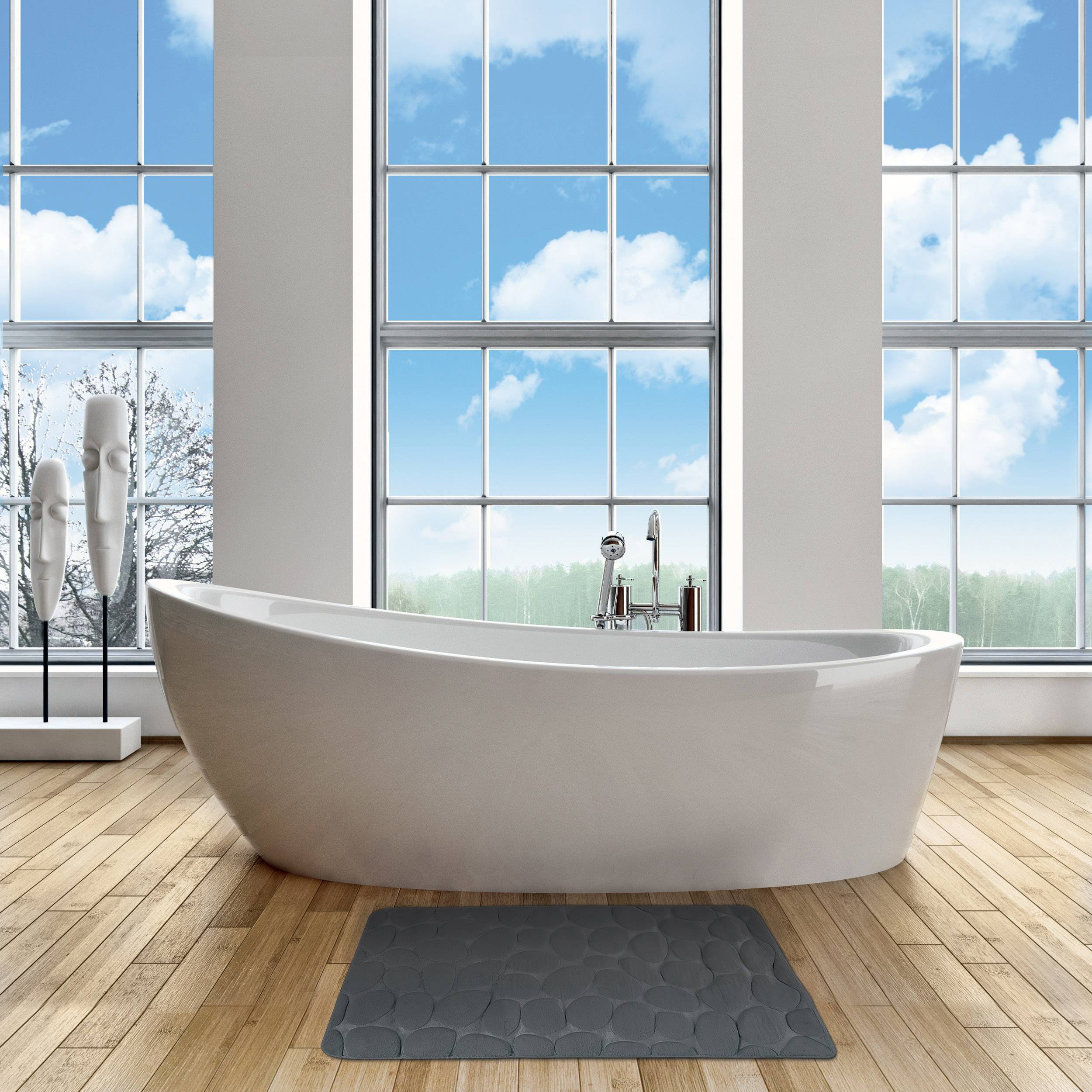 Modernes Badezimmer mit einer freistehenden weißen Badewanne, die vor großen Fenstern zentriert ist, einer grauen Badewannenmatte und dekorativen Skulpturen auf der linken Seite.