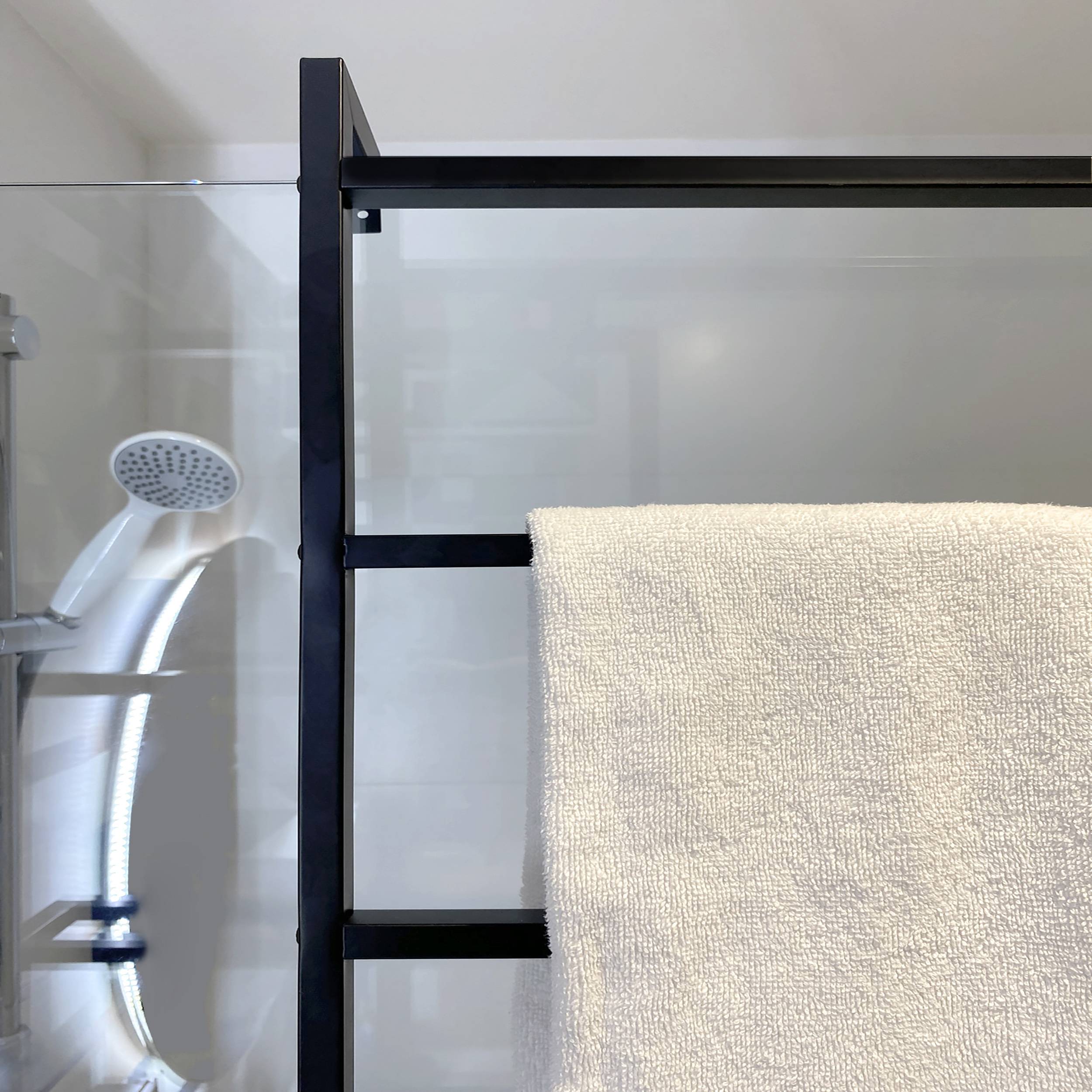 Badezimmerdusche mit Glastrennwand, schwarzem Handtuchhalter und einem cremefarbenen Handtuch, das auf der rechten Seite hängt.