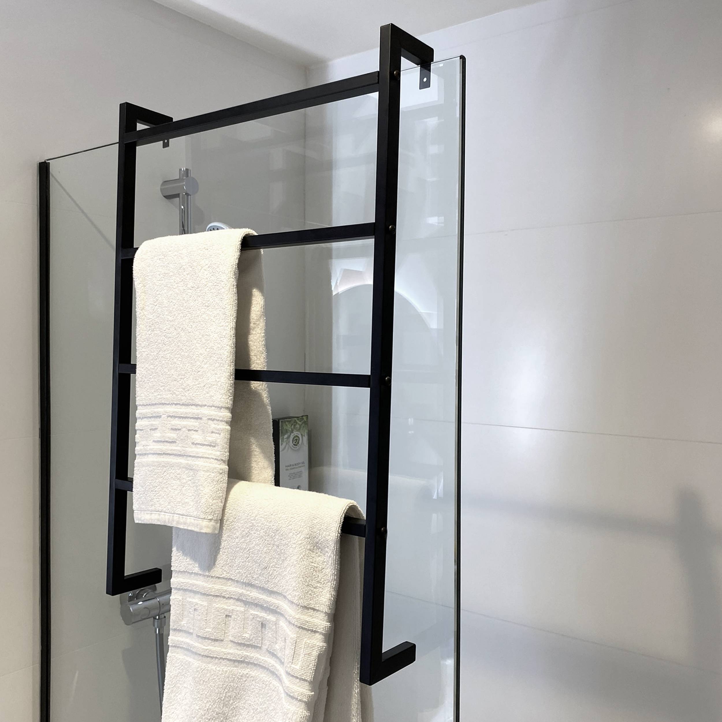 Schwarzer Metall-Duschpanel aus Glas mit zwei weißen Handtüchern, die daran hängen, in einem modernen gefliesten Badezimmer.