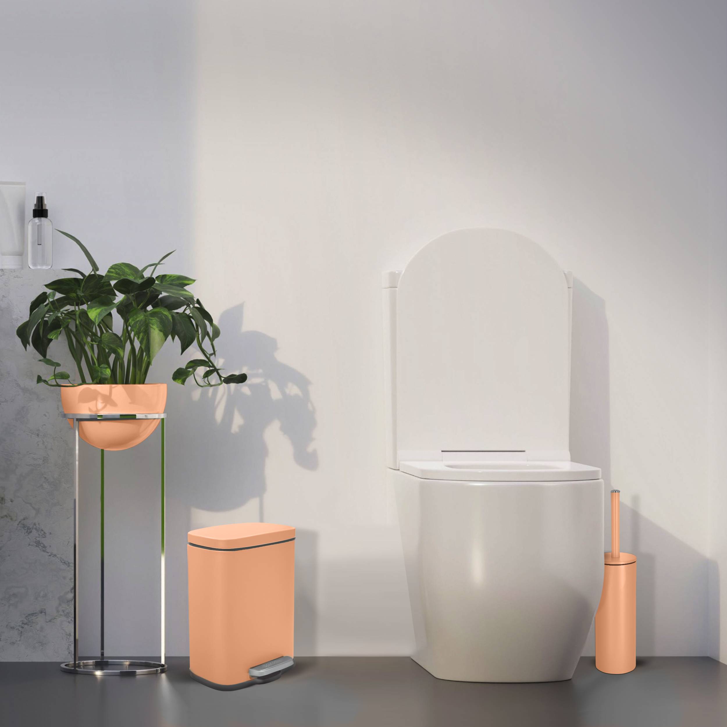 Minimalistisches Badezimmer mit einer weißen Toilette und einem Pfirsich-Mülleimer, Bürstenhalter und einer Topfpflanze auf einem Ständer vor einer schlichten Wand.
