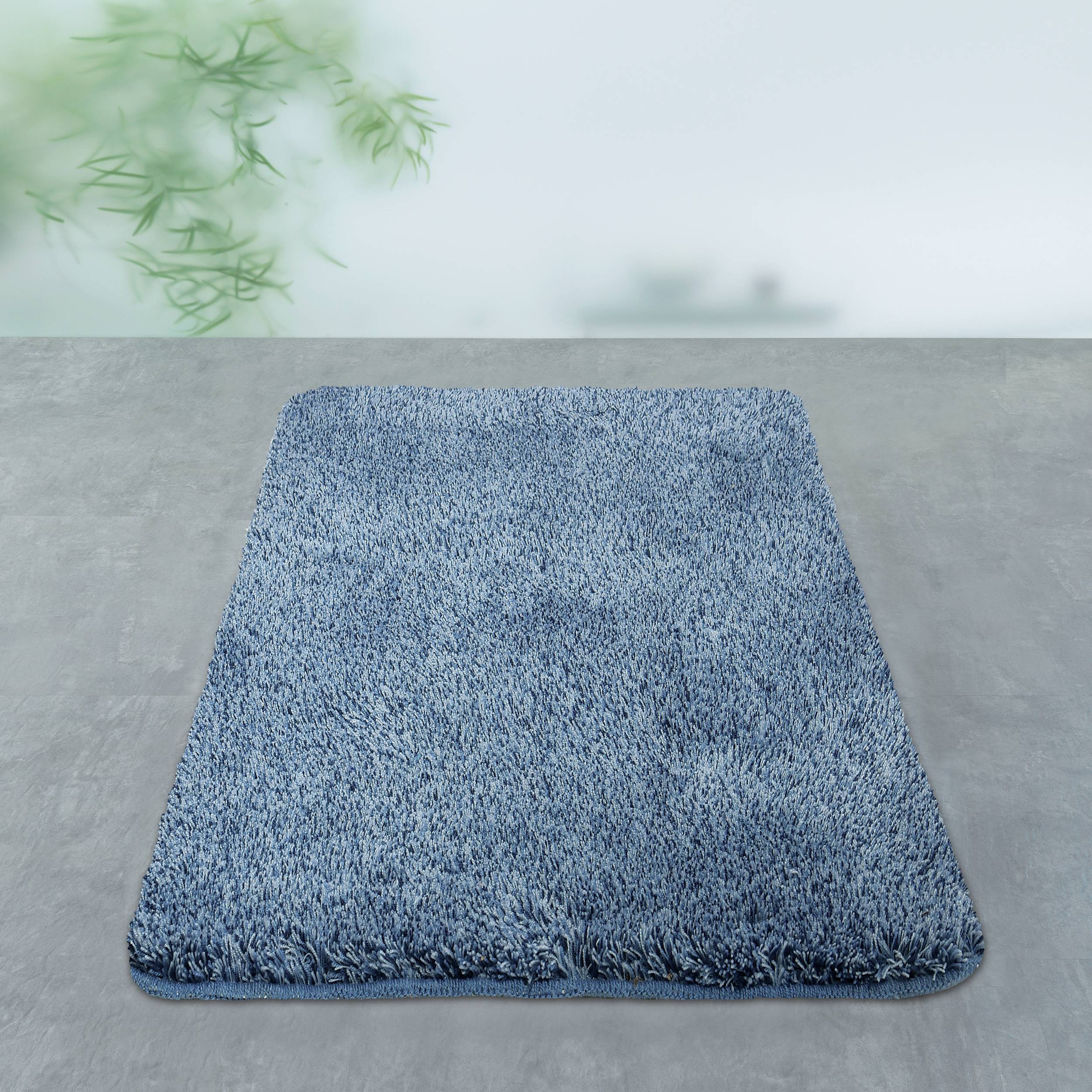 Blauer Hochflor-Teppich auf grauem Boden vor einer hellen Wand.