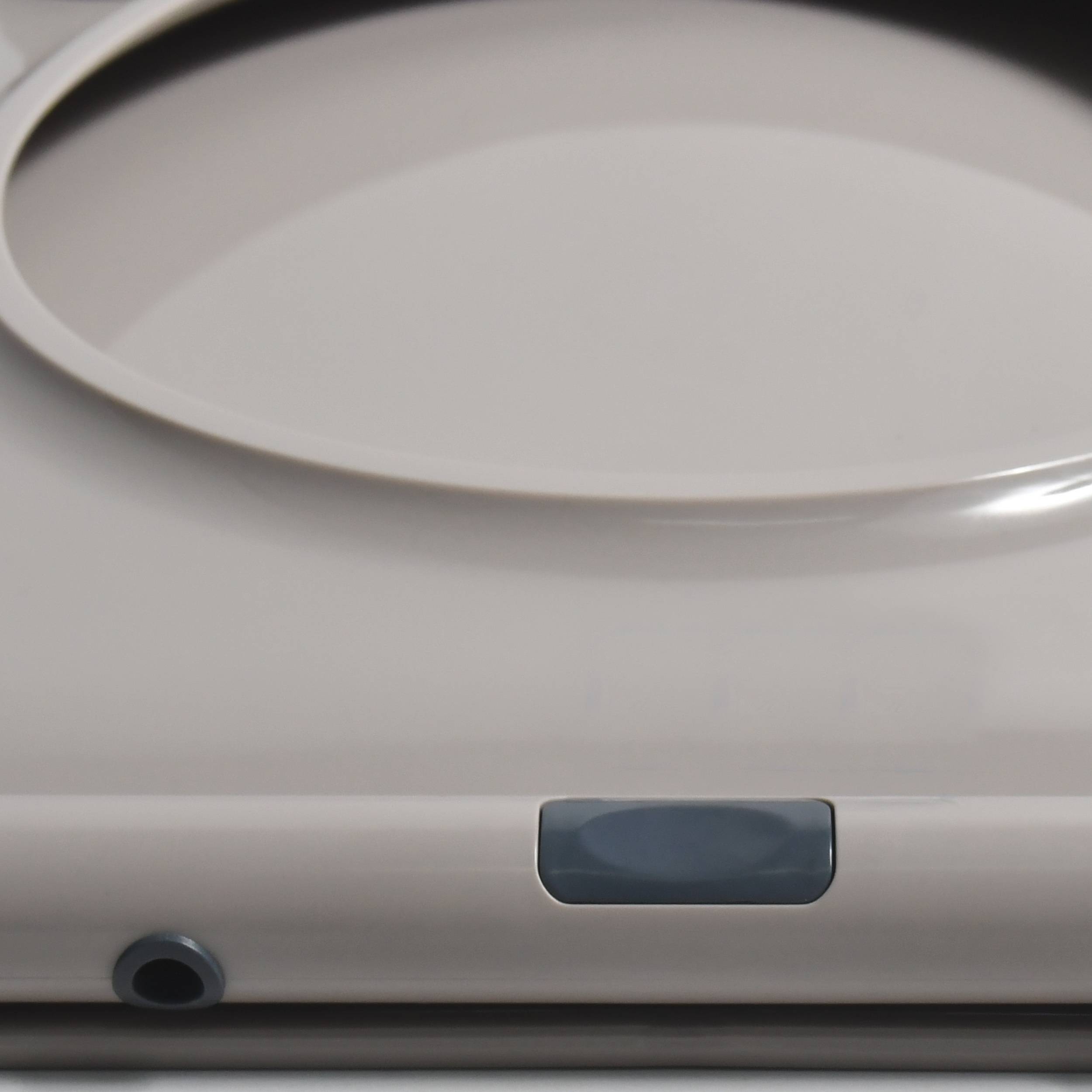 Nahaufnahme eines beigen elektronischen Geräts oder einer Haushaltsmaschine mit einem eingelassenen oberen Bedienfeld, einem dunklen rechteckigen Knopf und einer kleinen runden Öffnung auf der Vorderseite.