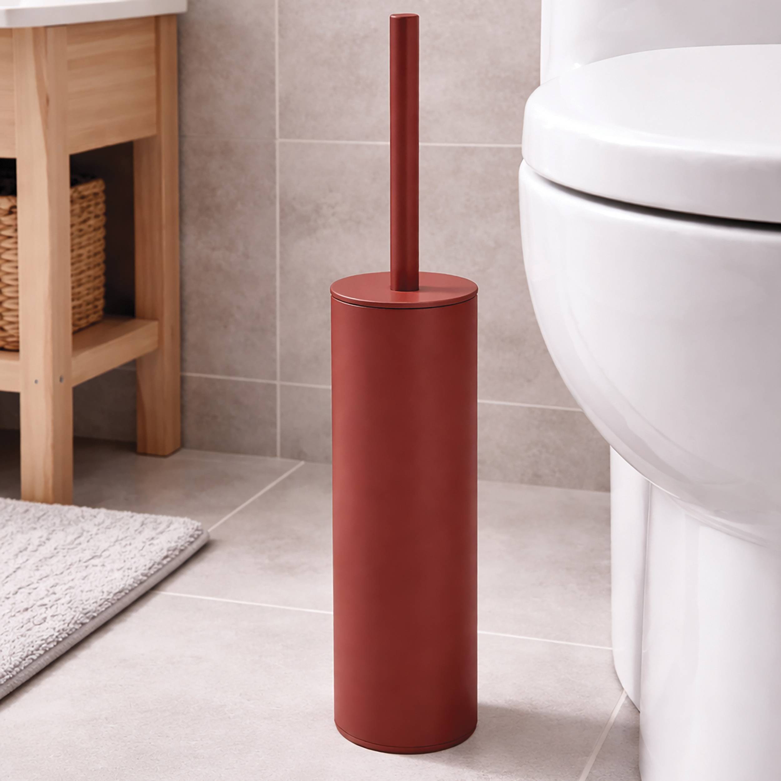 Roter Toilettenbürsten-Halter, der auf einem Badezimmerboden neben einer Toilette und einem Waschtisch steht.