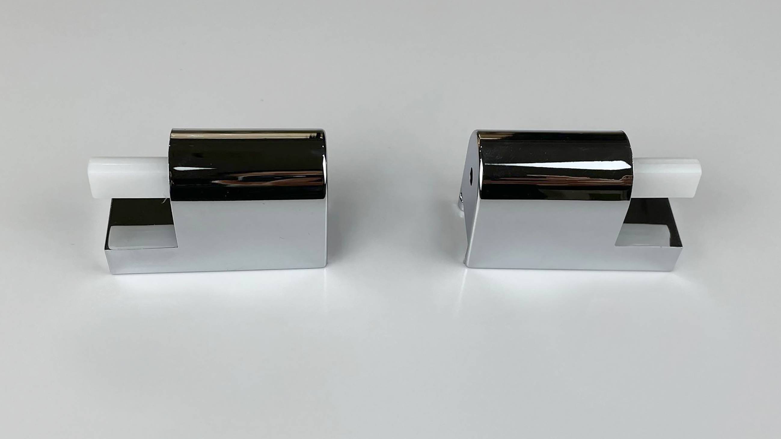 Zwei chrom- und weiße Glasklemmen oder Halterungen, die nebeneinander auf hellem Hintergrund gezeigt werden.