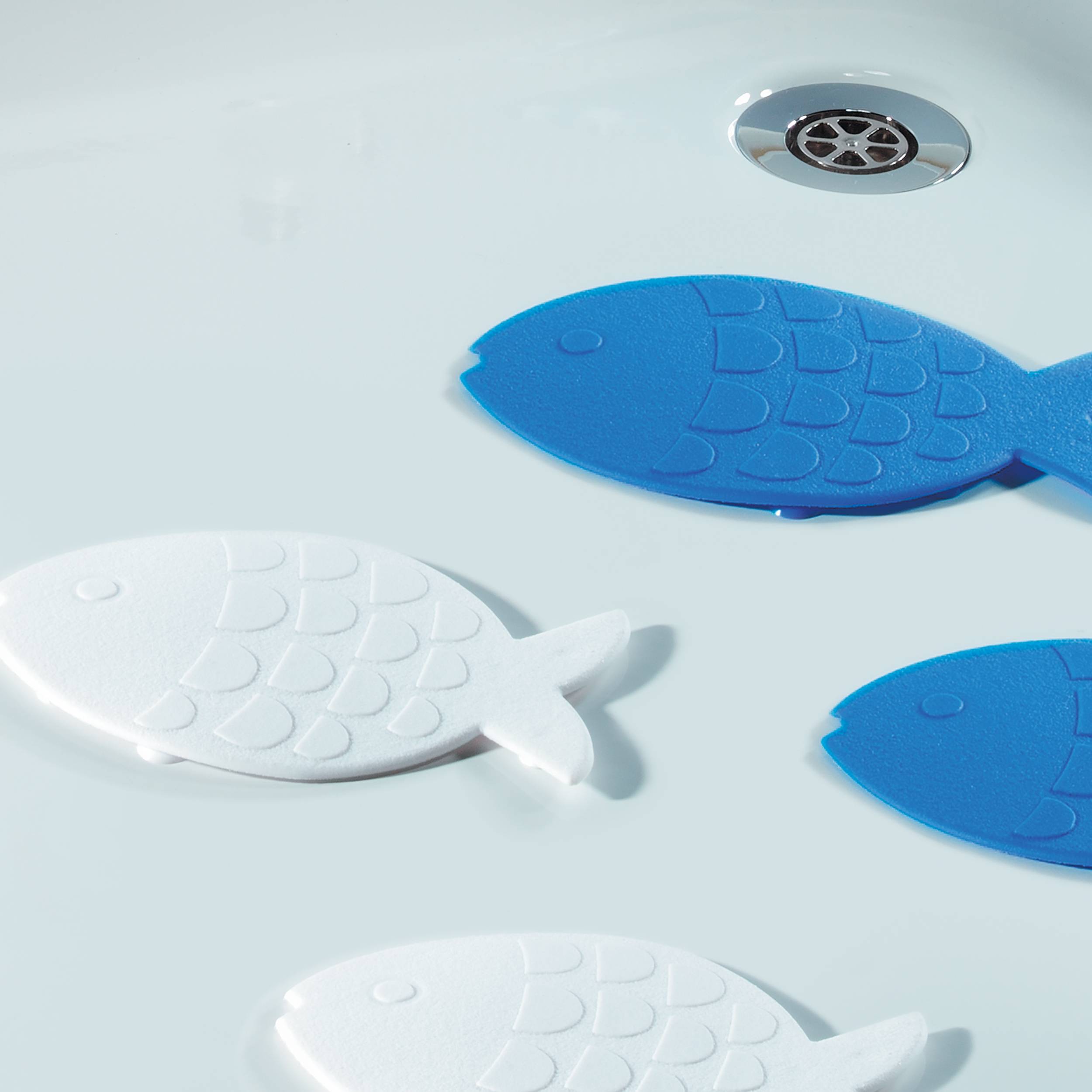 Drei fischförmige Badespielzeuge schwimmen in einer weißen Wanne in der Nähe eines Metallablaufs, zwei blau und eines weiß.