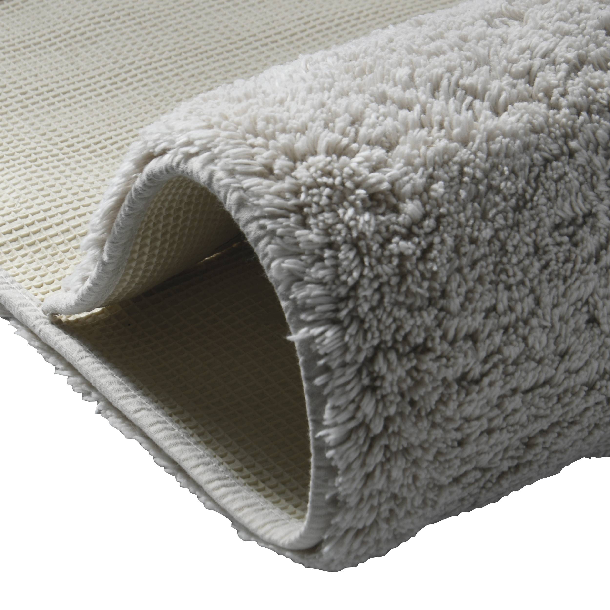 Nahaufnahme eines aufgerollten grauens Hochflor-Teppichs, die seine strukturierte Florhöhe und die beige Rückseite an der inneren Kante zeigt.