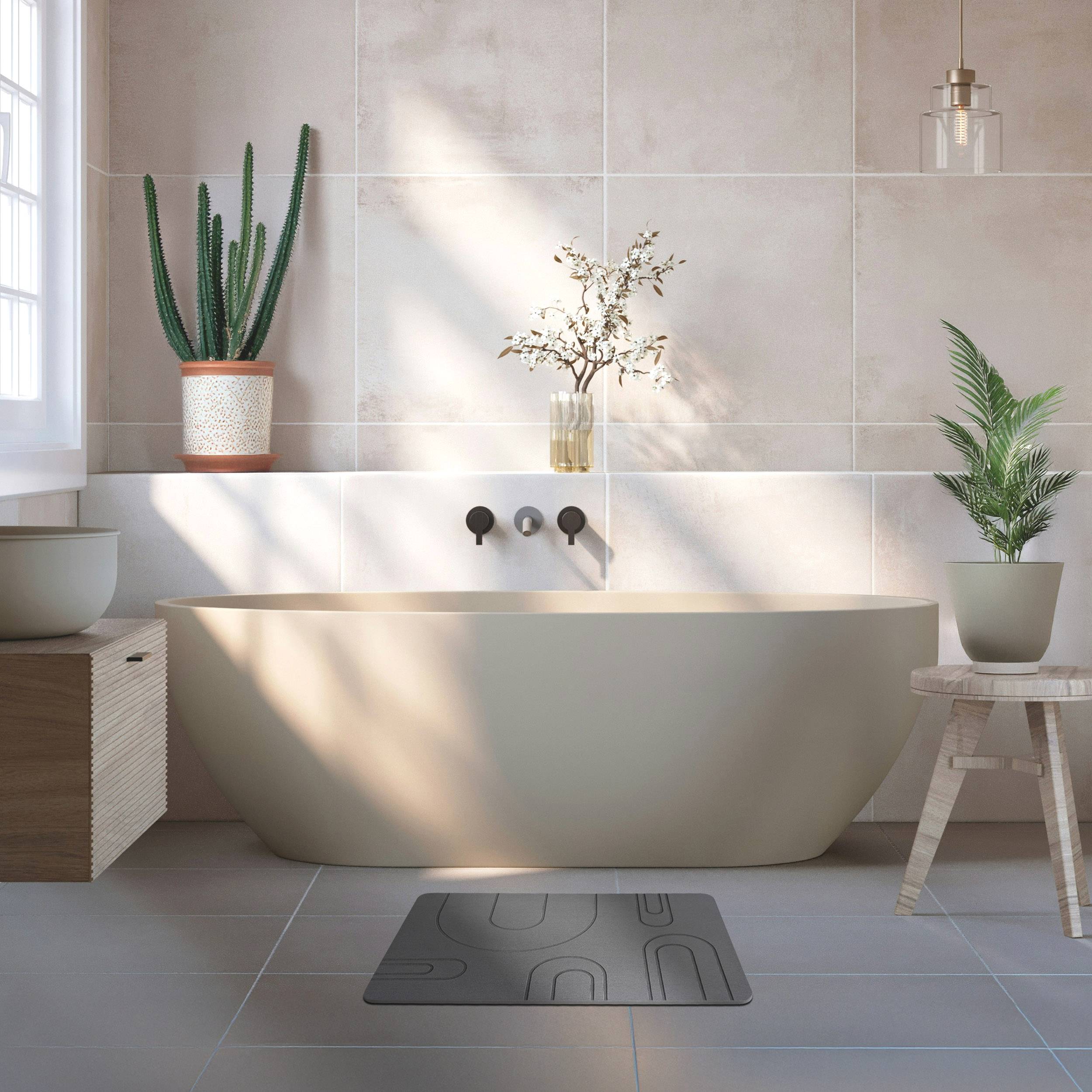 Minimalistisches Badezimmer mit einer freistehenden beigen Badewanne, Topfpflanzen, einem Hocker und sanftem Sonnenlicht, das Schatten über Fliesenw ände und -boden wirft.