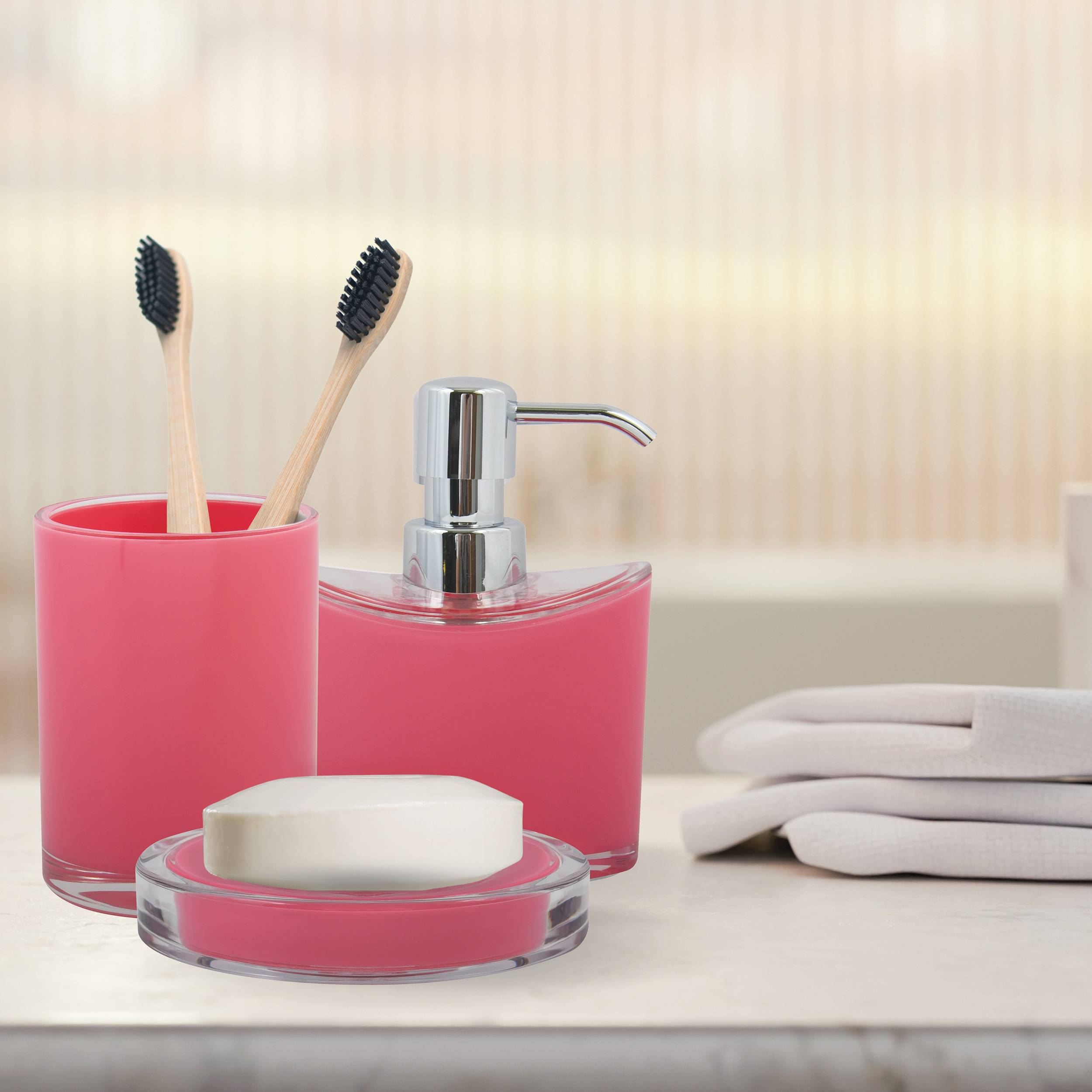 Rosa Badezimmeraccessoires auf einer Arbeitsplatte: Seifenspender, Zahnbürstenhalter mit zwei Zahnbürsten, Seifenschale und gefaltete Handtücher.
