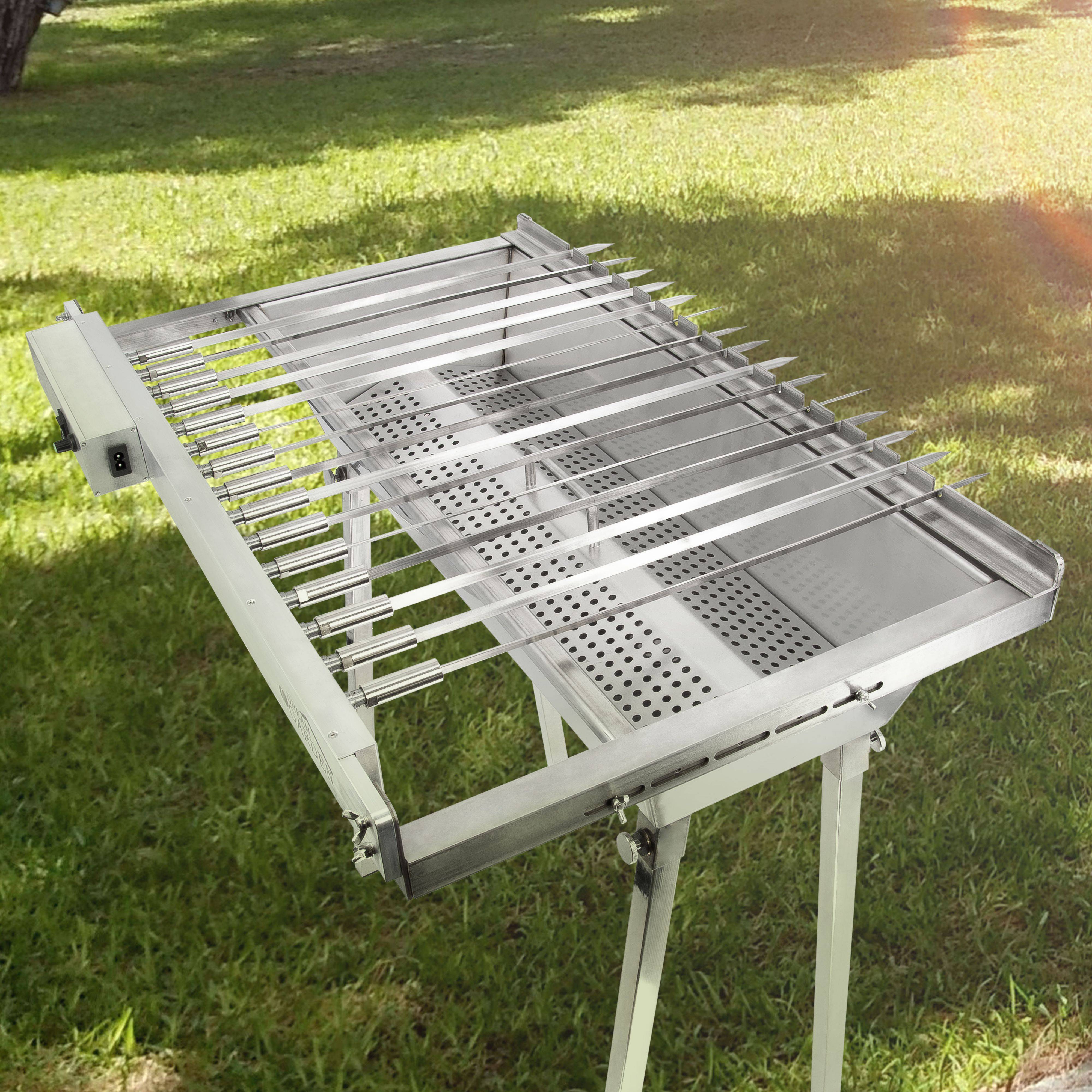 Edelstahl-Außengrill oder Kochrost mit verstellbaren Stangen, auf einem Ständer in einem grasbewachsenen Garten dargestellt.