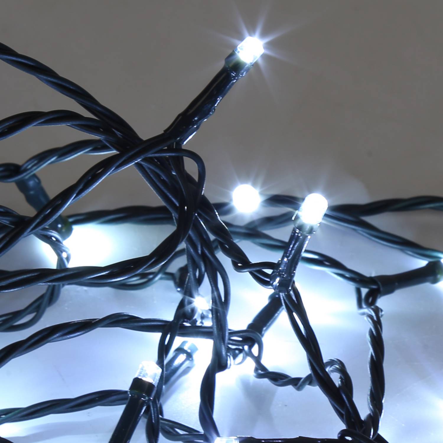 Nahaufnahme von verworrenen schwarzen Lichterketten mit mehreren kleinen weißen LEDs, die gegen einen einfachen Hintergrund leuchten.