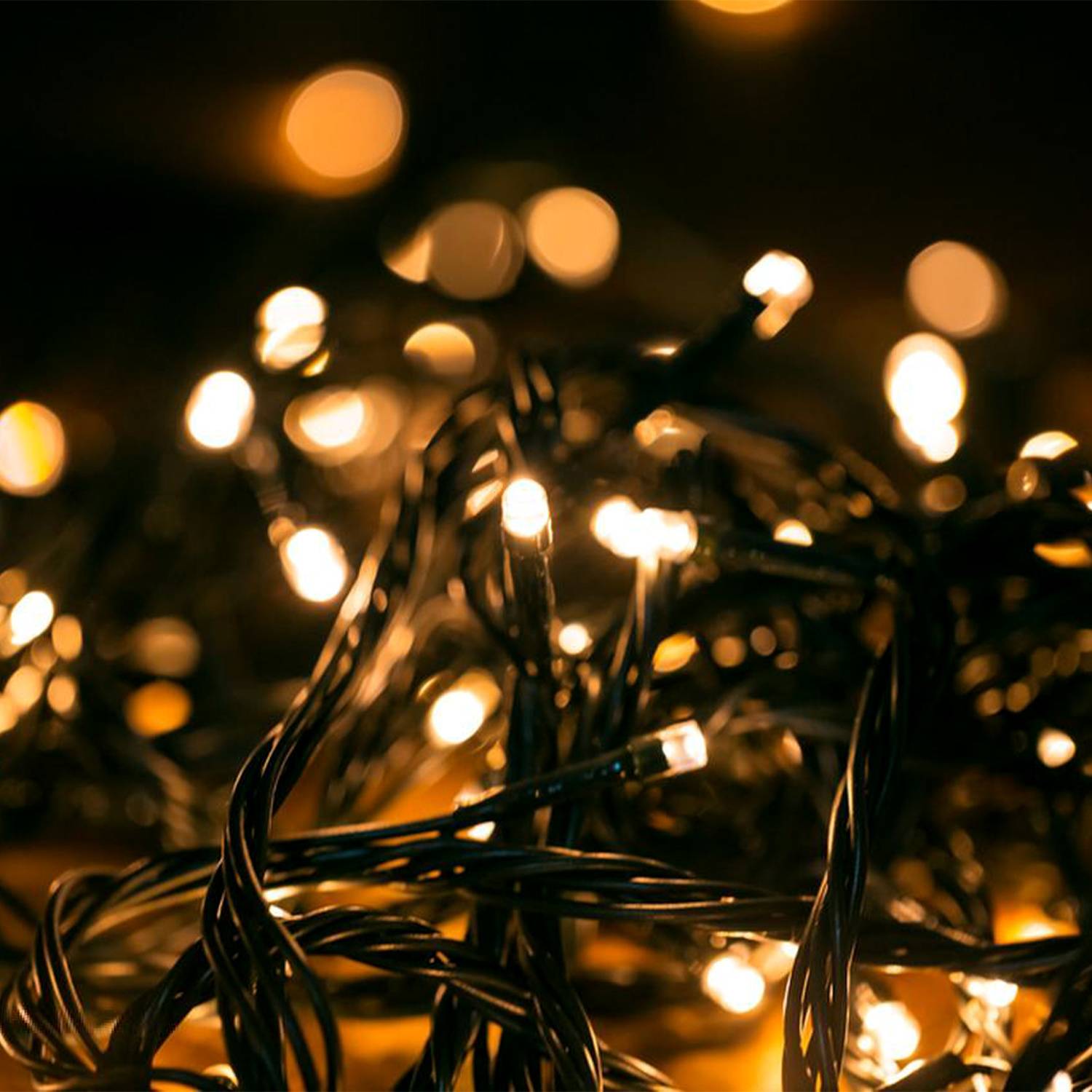 Verdrehte schwarze Lichterketten, die in warmem Gelb gegen einen dunklen Hintergrund leuchten, mit unscharfen Bokeh-Lichtern dahinter.