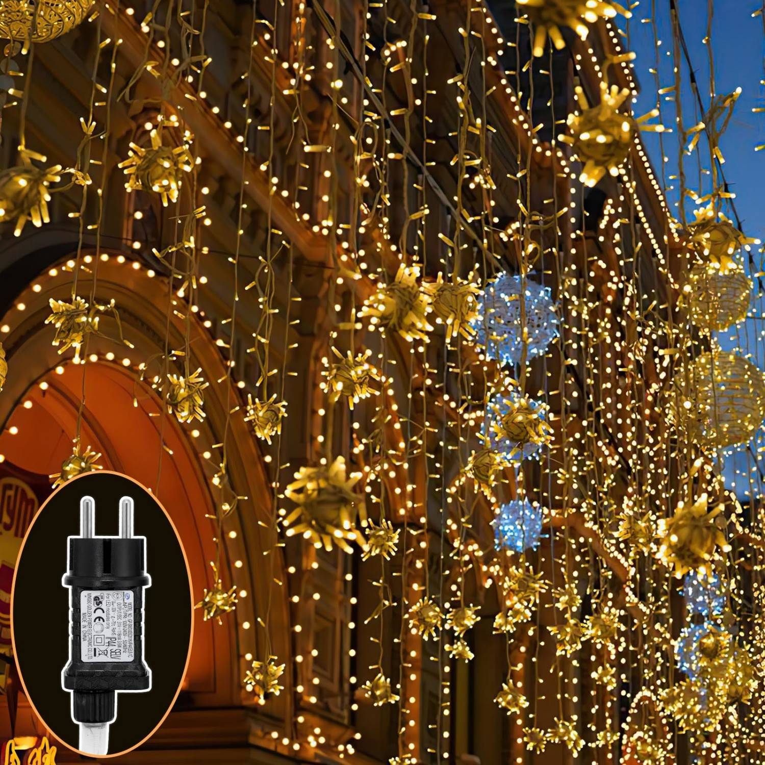 Goldene, sternförmige Lichter, die nachts über eine Gebäudefassade drapiert sind, mit einem eingefügten Bild eines schwarzen Stromsteckers oder Stromadapters.