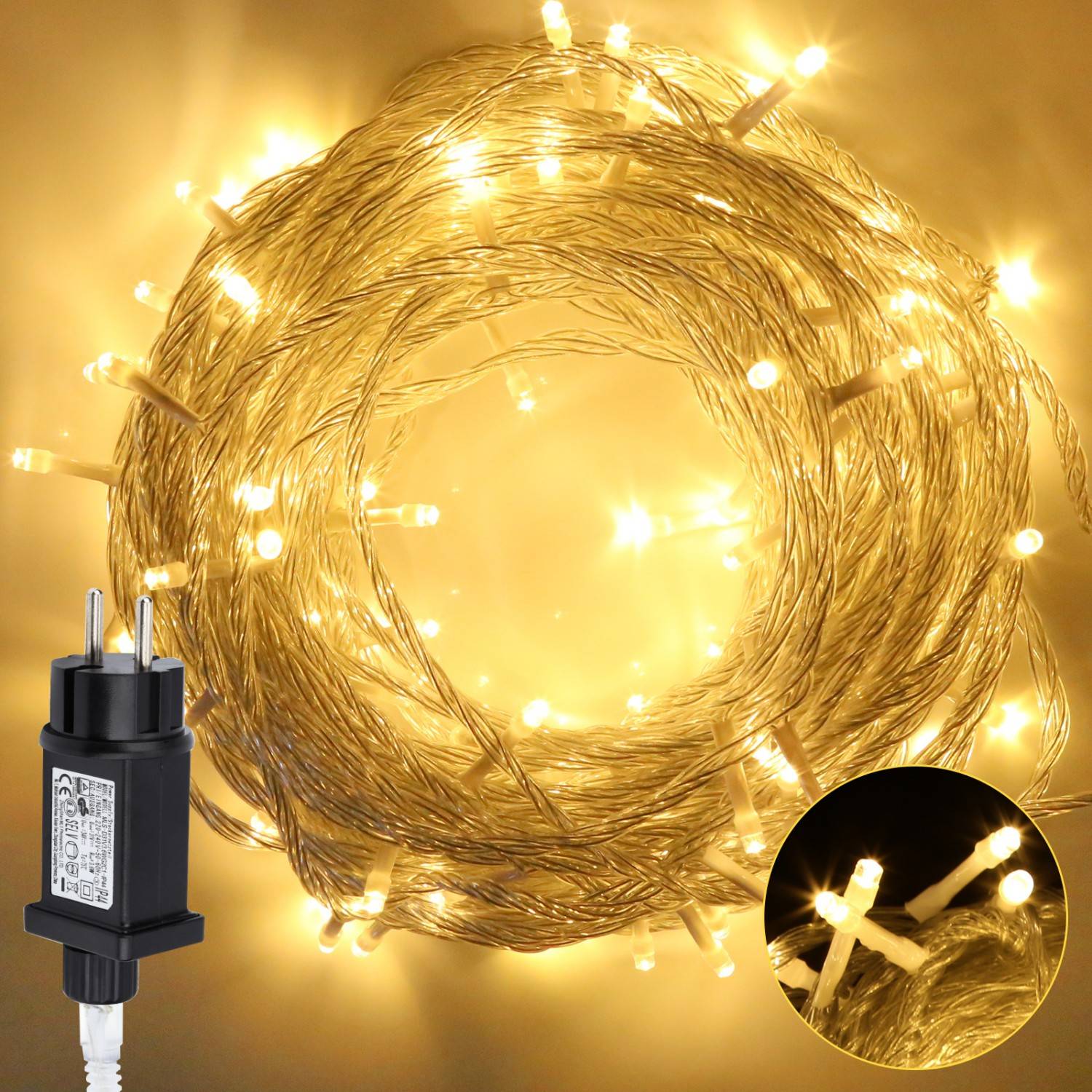 Aufgerollte warmweiße Lichterkette, angeschlossen an einen schwarzen Stromadapter, mit einer Nahaufnahme des Lichterstrangs in einer Bildeinblendung.