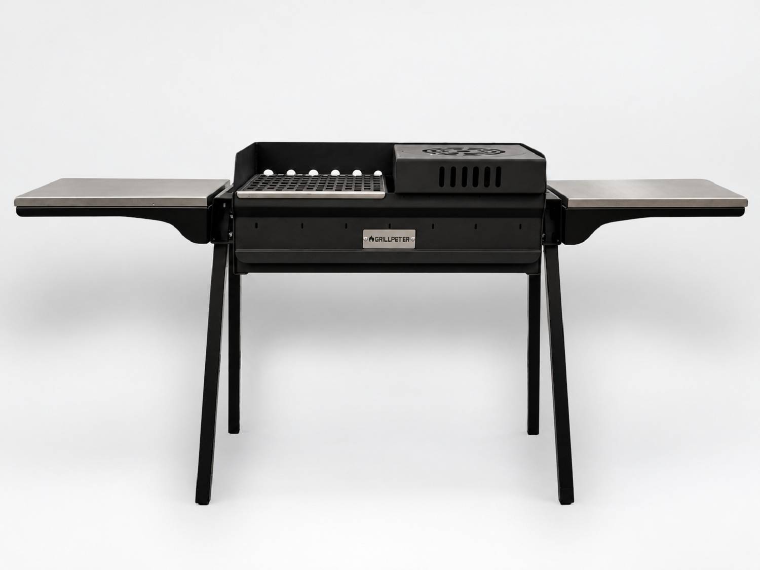 Tragbarer schwarzer Holzkohlegrill mit Seitenablagen und Deckel, Vorderansicht auf weißem Hintergrund.