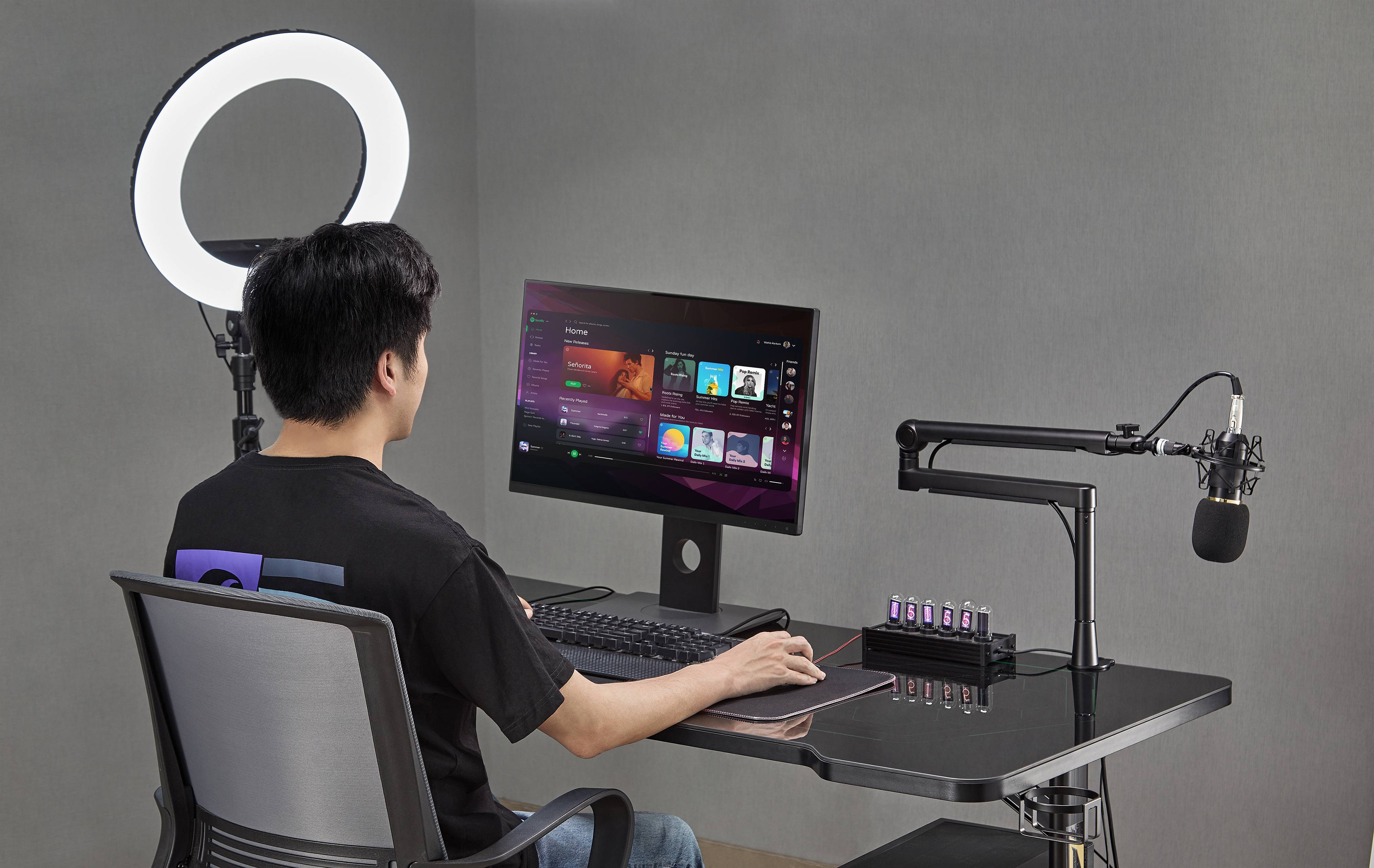 Person an einem Schreibtisch, der einen Desktop-Computer mit Ringlicht und Mikrofon nutzt, eingerichtet zum Streamen oder Podcast-Aufnahmen.