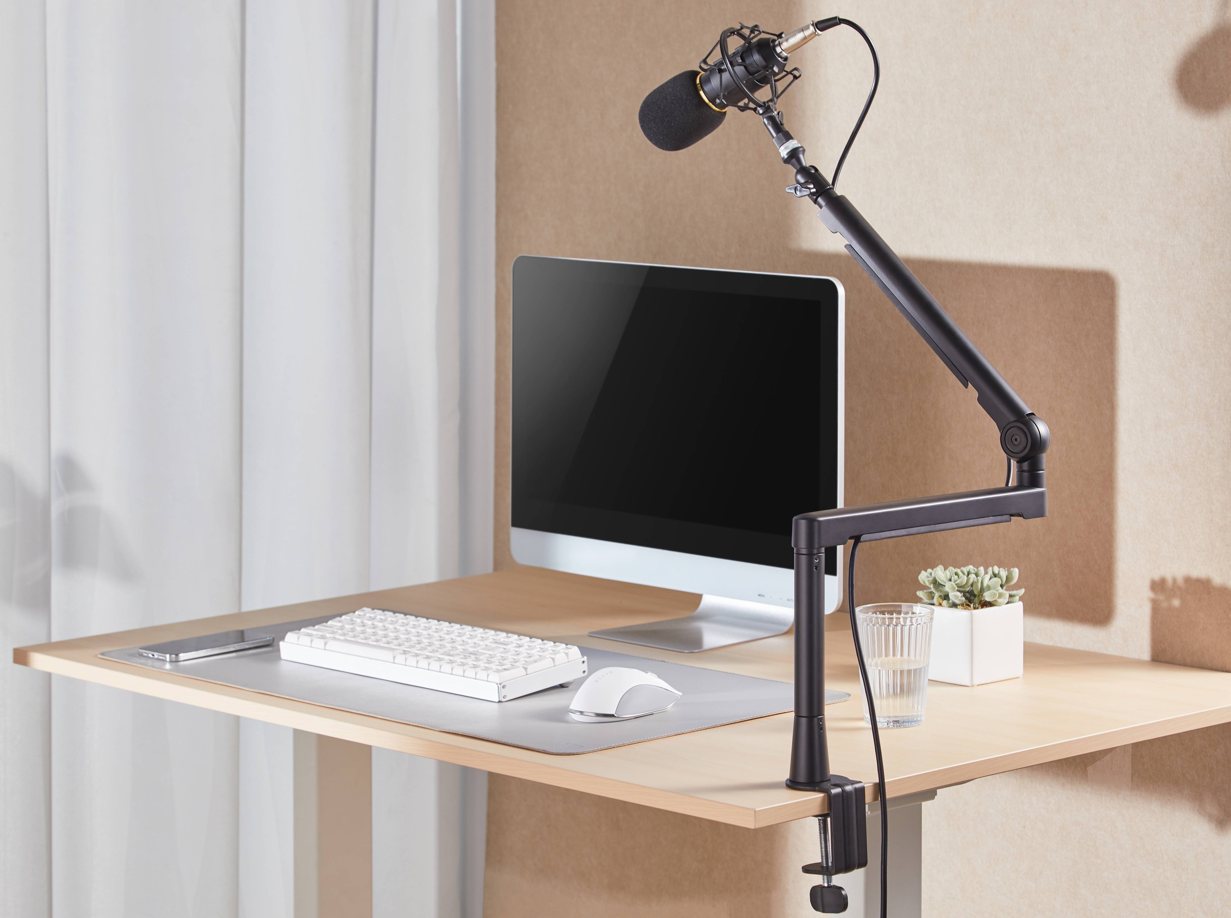 Minimalistischer Home-Office-Schreibtisch mit iMac, Tastatur, Maus und Boom-Mikrofon, was auf ein Podcasting- oder Aufnahmeset-up hindeutet.
