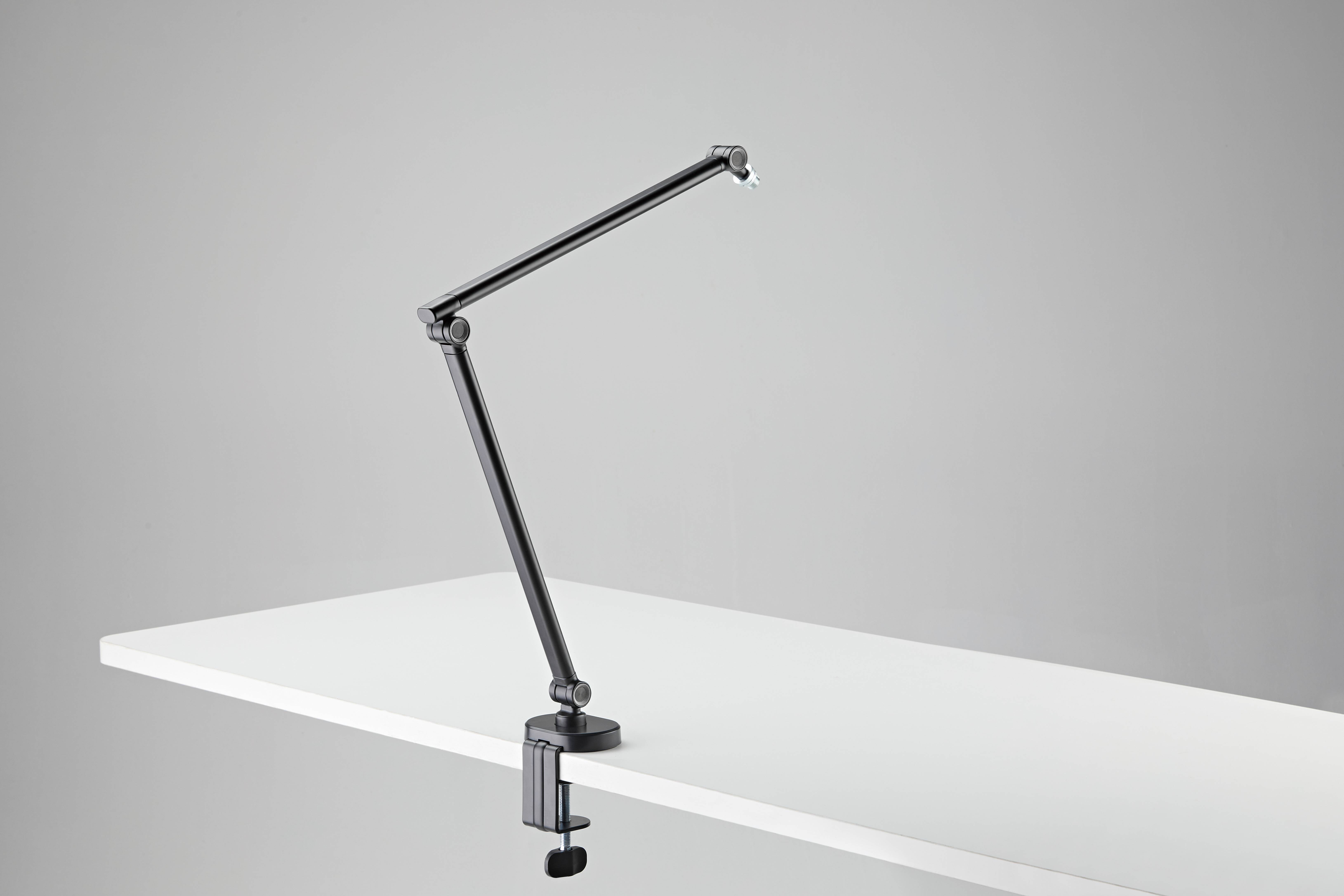 Schwarze verstellbare Schreibtischlampe, die an der Kante einer weißen Tischplatte gegen einen grauen Hintergrund geklemmt ist.