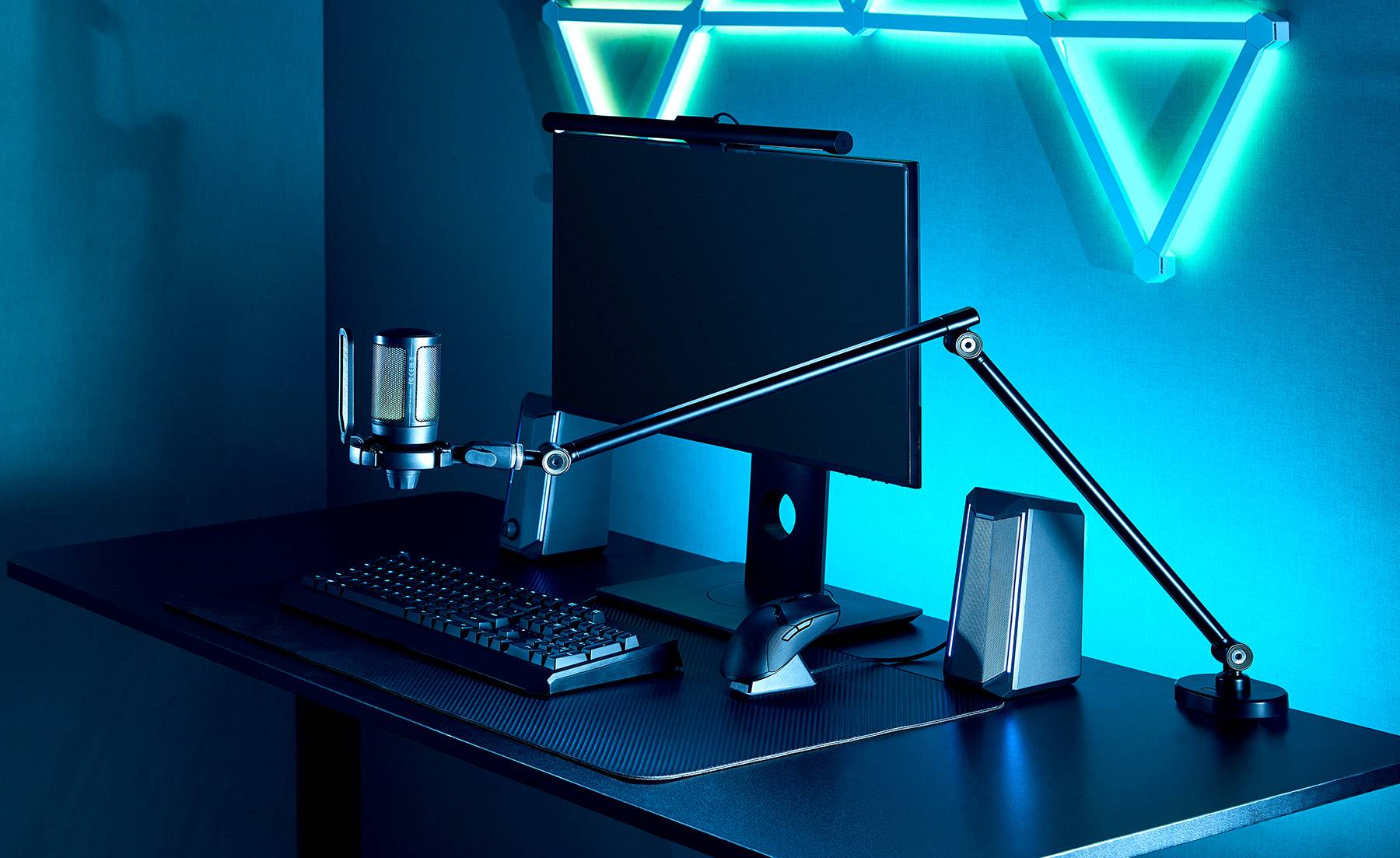 Ein dunkles, minimalistisches Schreibtisch-Setup mit einem Monitor, einer Tastatur, einem Mikrofon und einer verstellbaren Schreibtischlampe, beleuchtet durch blaue Neon-Wandakzente.