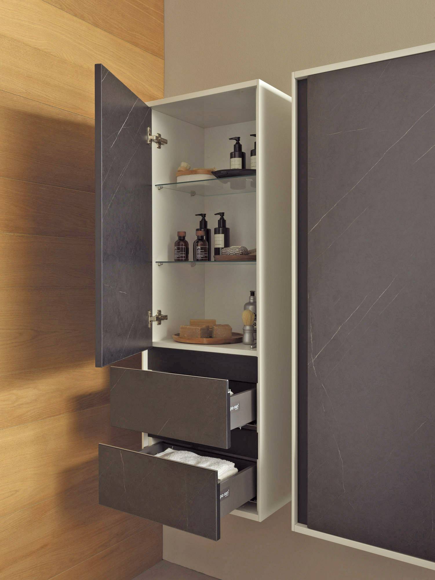 Offener Badezimmerschrank an der Wand mit Spiegeltür, Regale mit Toilettenartikeln und zwei herausgezogene Schubladen mit Handtüchern.