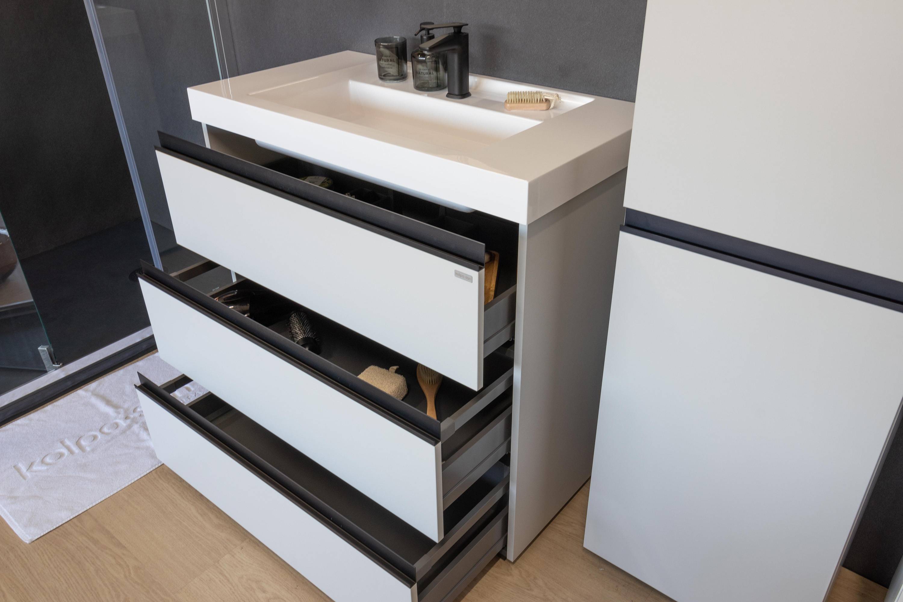 Moderner Waschtischschrank mit offener oberer Schublade, die organisierte Lagerung unter einer weißen Spülenarbeitsplatte in einem Badezimmer zeigt.