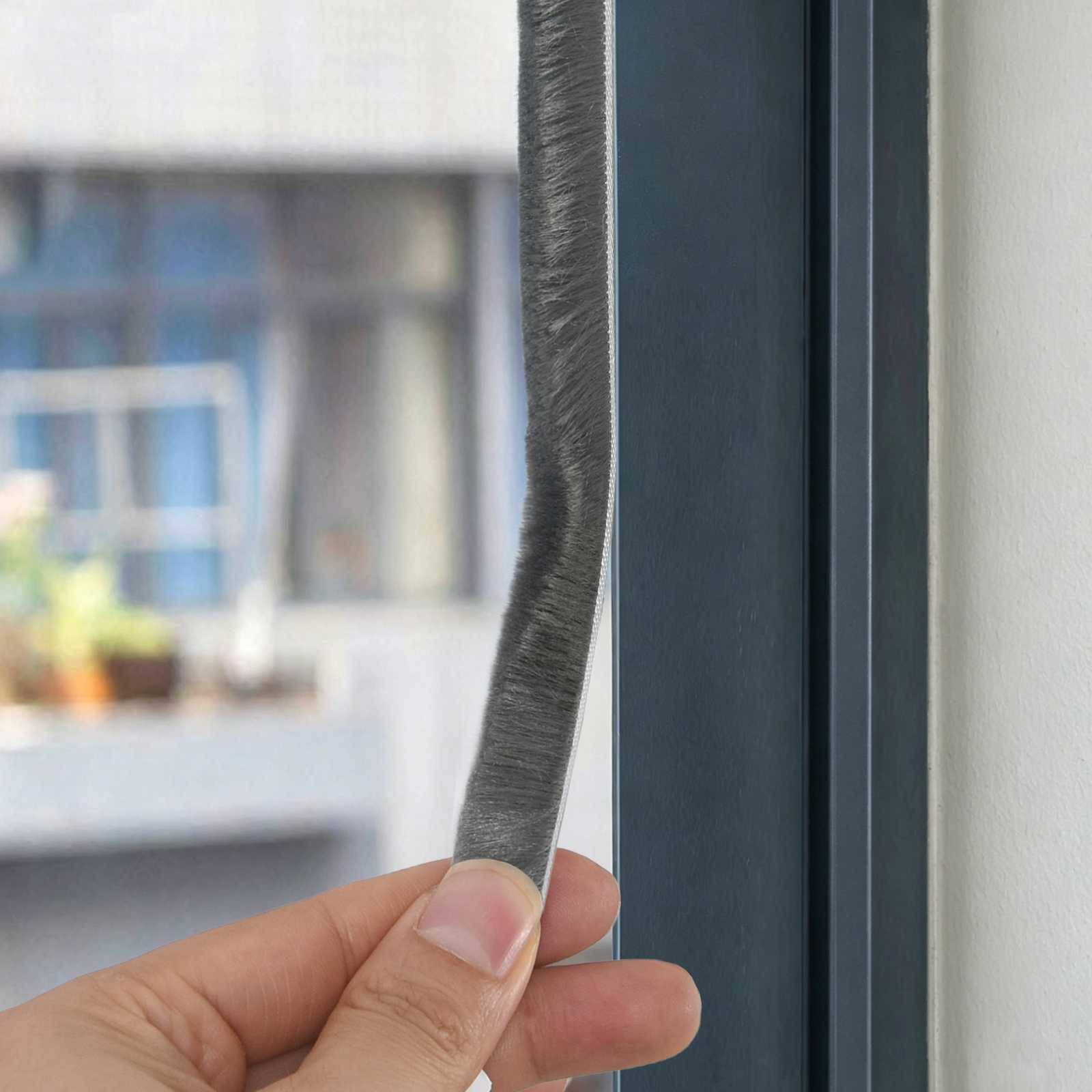 Hand, die eine schmale Dichtungsleiste neben einen Fensterrahmen hält, was auf Installation oder Austausch zur Isolierung hindeutet.