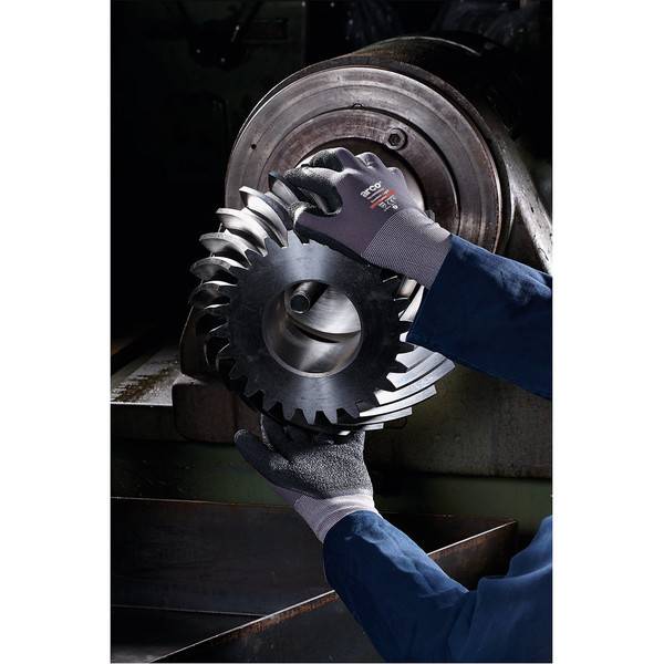 Handschuhgetragener Arbeiter, der ein großes Metallgetriebe vor einer Industriemaschine hält, was eine Inspektion oder Bearbeitung andeutet.