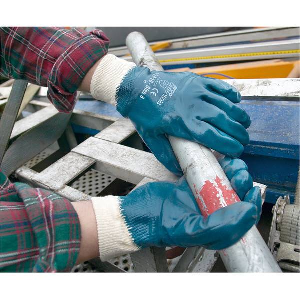 Handschuhgetragener Arbeiter hält und inspiziert ein Metallrohr oder eine Metallstange über einer Industrieanlage.