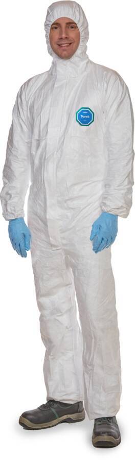 Eine Person, die einen weißen Einweg-Schutzanzug, eine Kapuze, blaue Handschuhe und Arbeitsschuhe trägt, ist vor einem einfachen Hintergrund zu sehen.