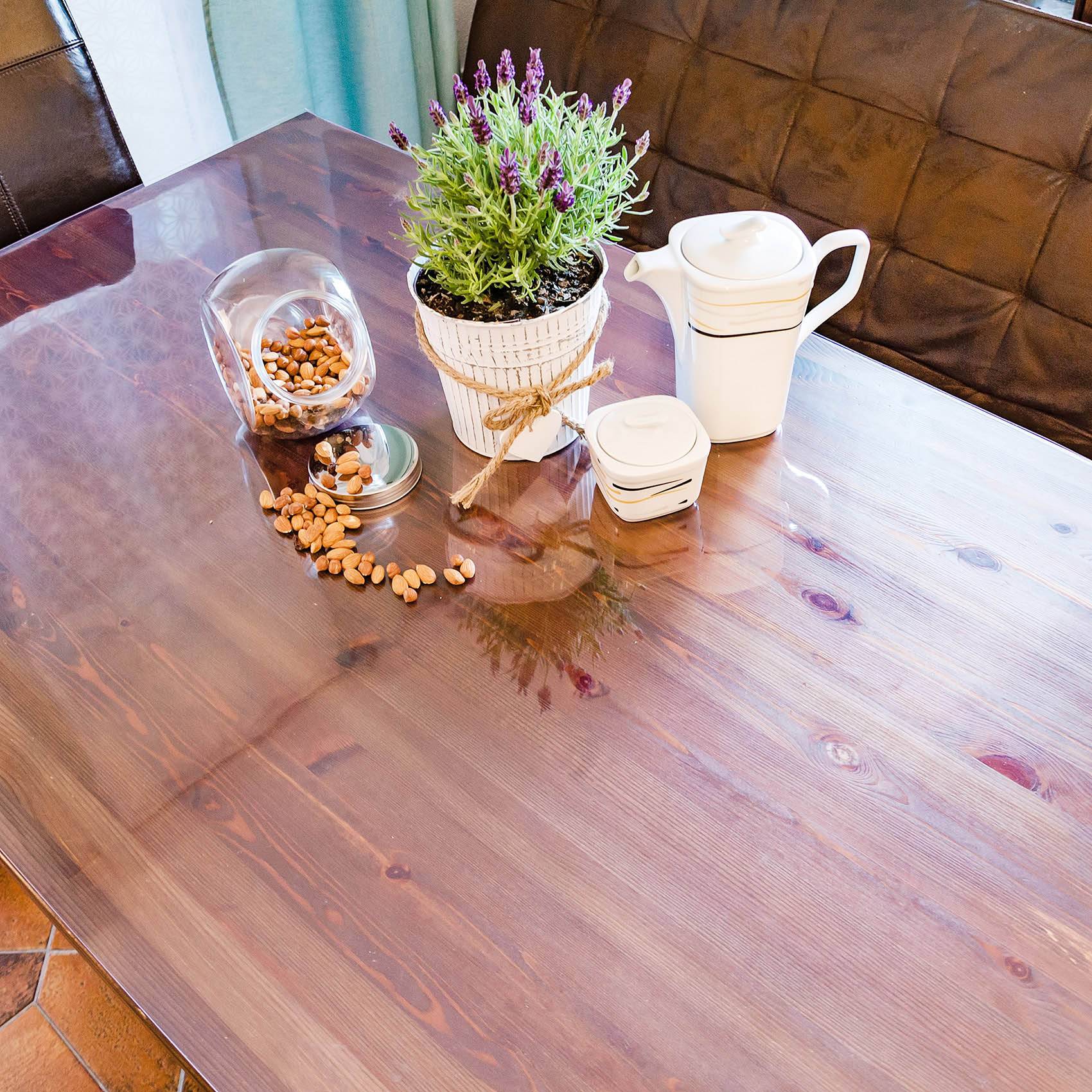 Holztisch mit einer Topflavendelpflanze, weißer Teekanne und Tasse sowie einem Glasgefäß mit Nüssen, die auf die Oberfläche verschüttet werden.