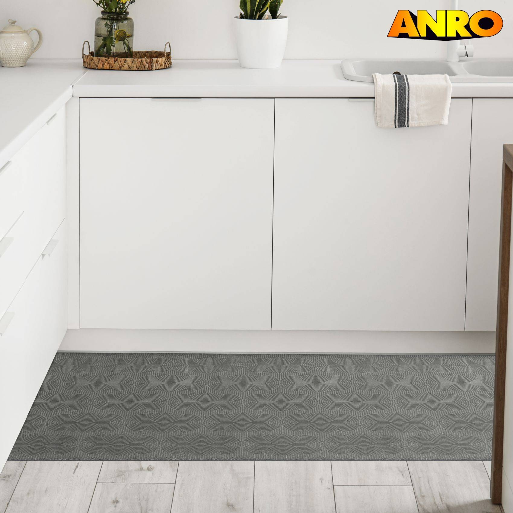 Weiße Küche mit eingebauten Schränken, Arbeitsplatte mit Dekoration, Spülenbereich und eine graue gemusterte Bodenmatte auf hellem Holzfußboden.