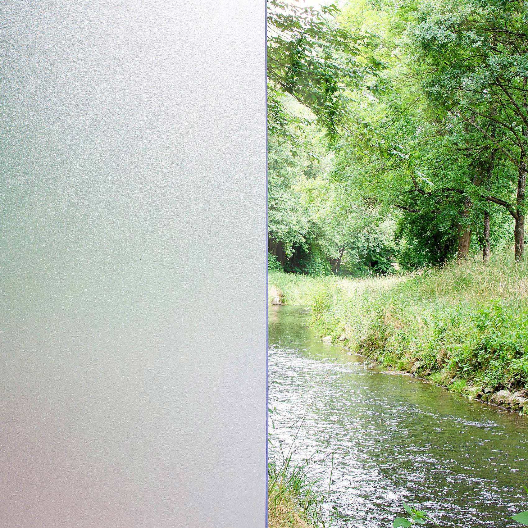 Ein reflektierendes Milchglaspaneel auf der linken Seite und ein ruhiges, mit Bäumen gesäumtes Flussufer auf der rechten Seite, mit grünem Gras und überhängenden Bäumen.