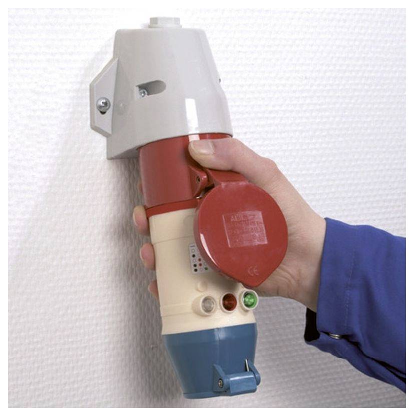 A hand in a blue sleeve grips a large industrial plug with a red, white, and blue color scheme, mounted on a white wall.
