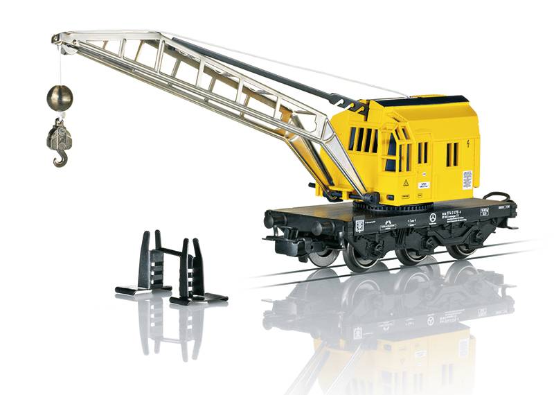 A model train crane car with a yellow cabin and extendable metal boom, featuring a hook and ball for lifting. Placed on reflective surface.