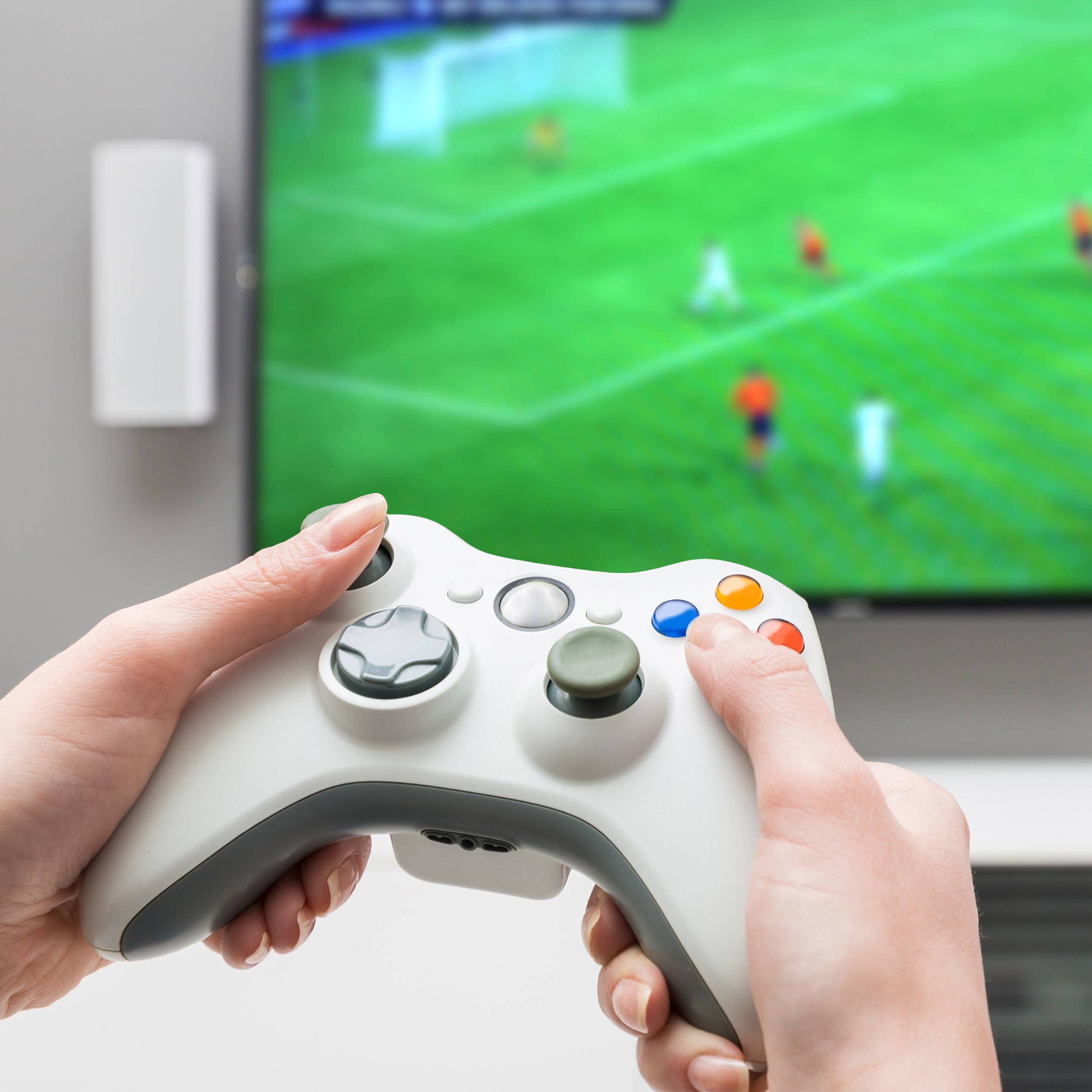 A person is playing a sports video game on a console. A controller can be seen in their hands, with the game displayed on a screen.