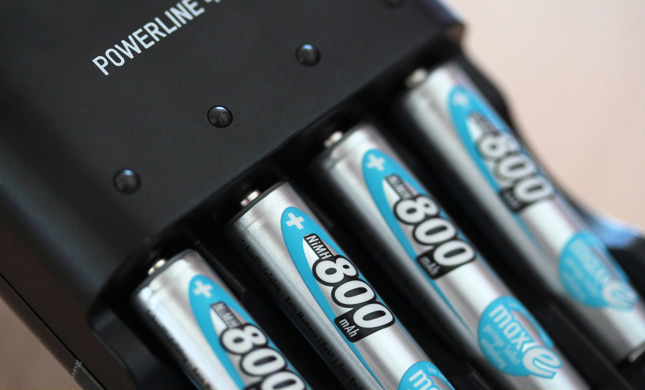 A battery charger is charging four rechargeable AA batteries with blue and silver labels. At the top, it reads 'POWERLINE 4 LIGHTS'.