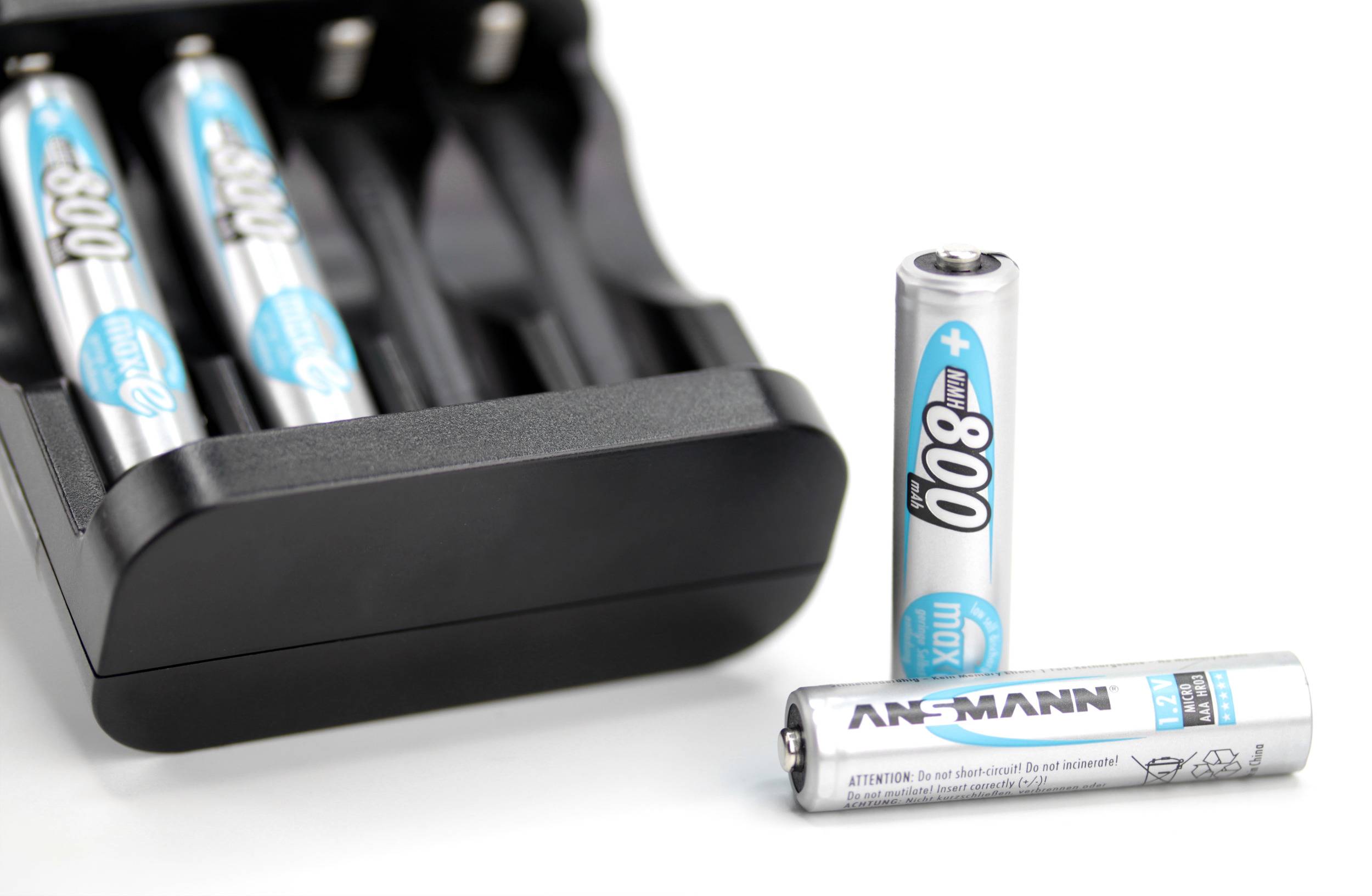 A battery charger is partially filled with blue-and-white AA batteries; another battery lies in front of it.