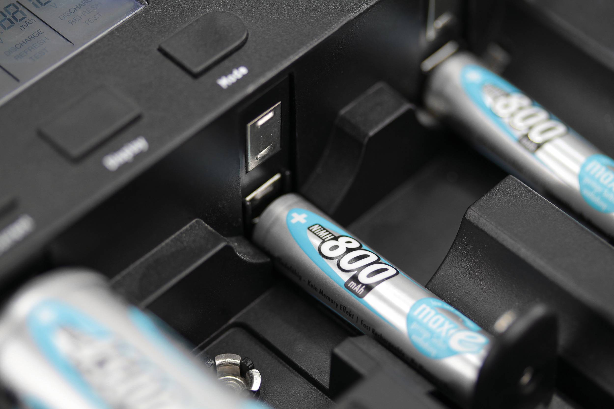 Battery charger with multiple rechargeable AA batteries being charged; focus on one battery in one of the charging slots.