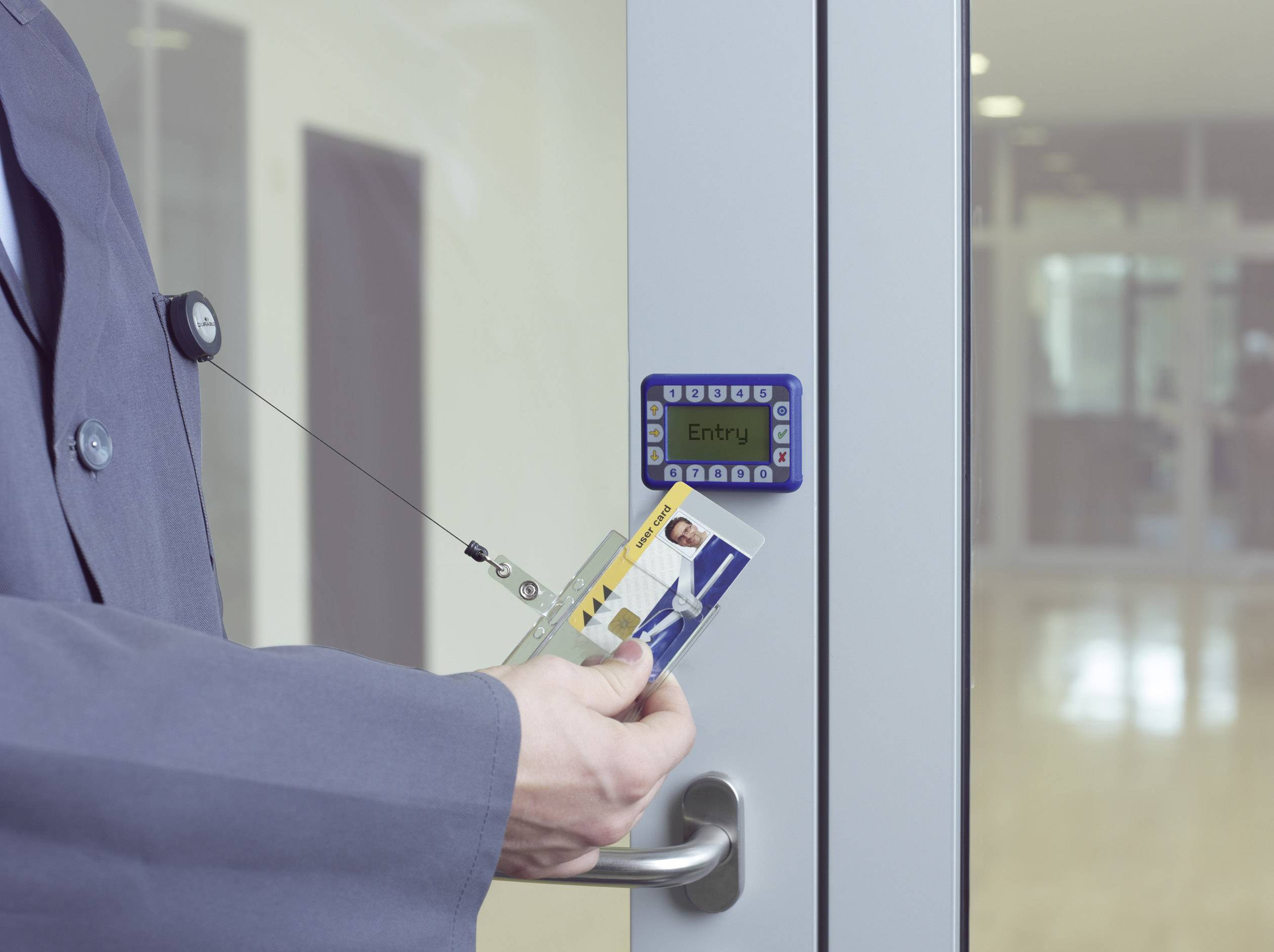 A person holds an RFID card up to an access control device on a glass door to gain entry to a building.