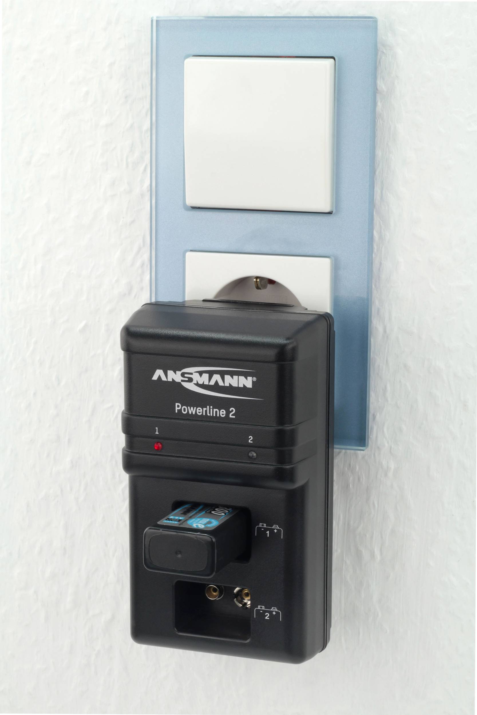 A charger by Ansmann is plugged into a wall socket and is charging a battery.