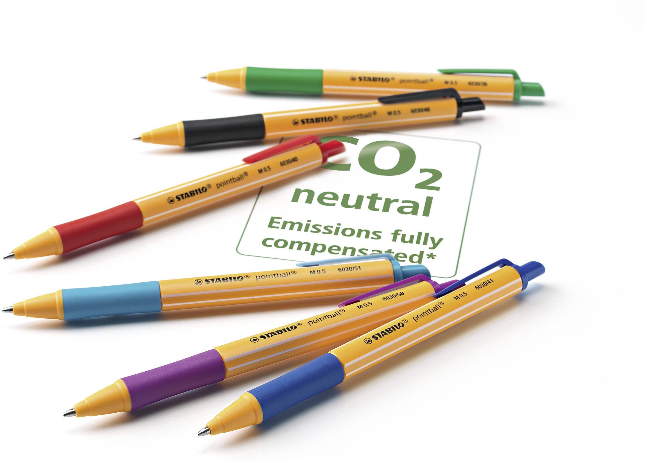 Six pens in different colours lie on a sheet of paper. On the paper it reads: 'CO₂ neutral Emissions fully compensated'.
