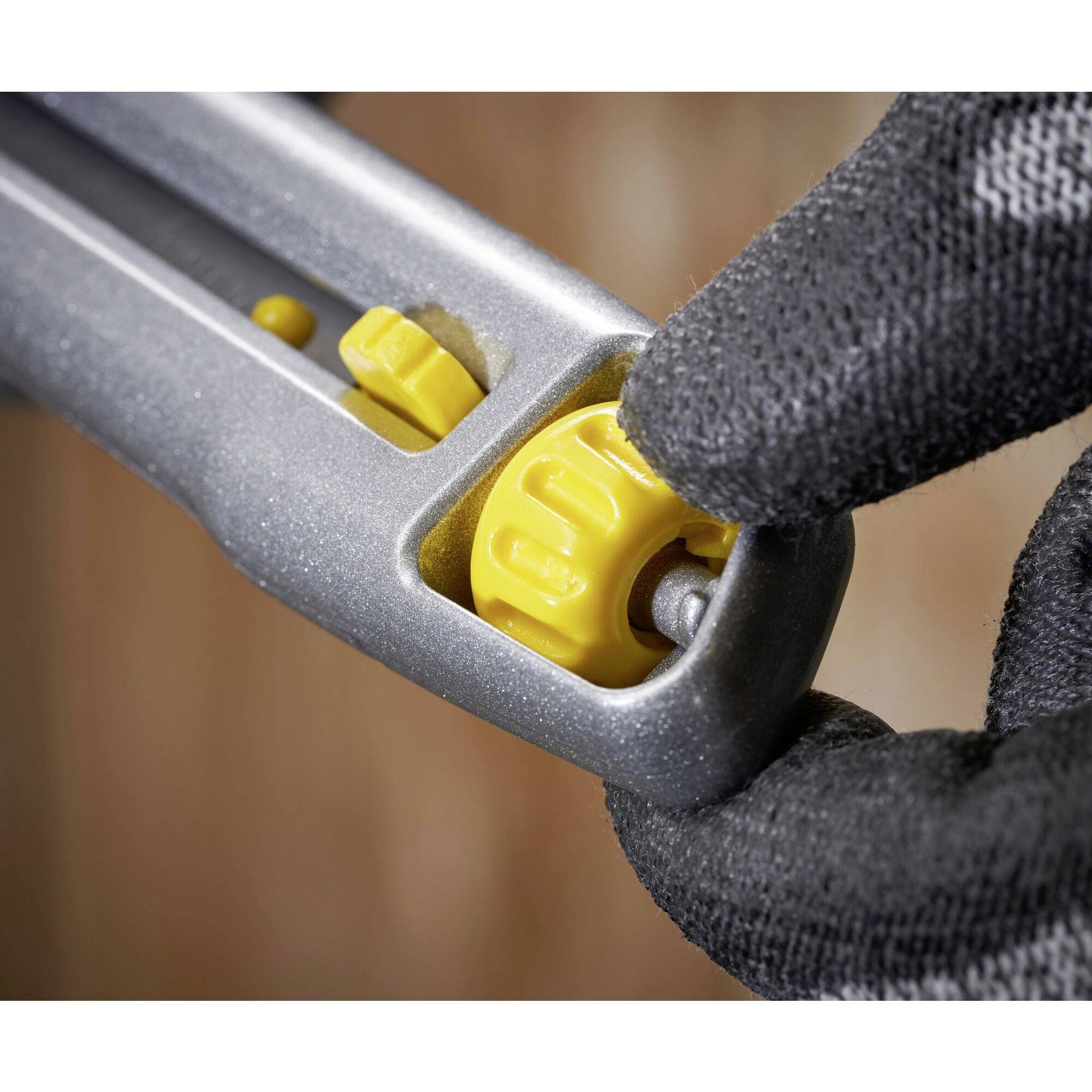 Two hands wearing black gloves are holding a grey tool with a yellow adjustment dial. Focused on fine-tuning.